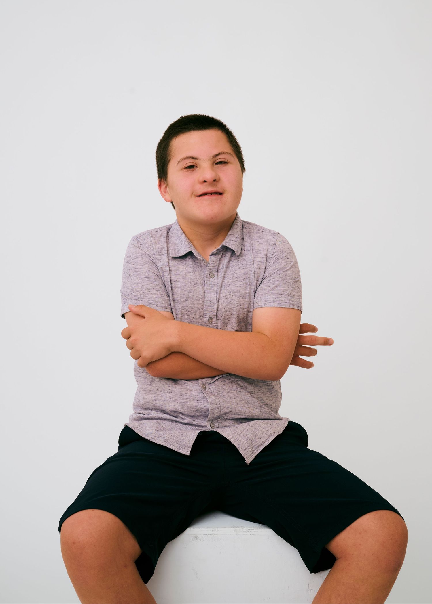 Person in grey polo shirt and black shorts sits casually against white background.