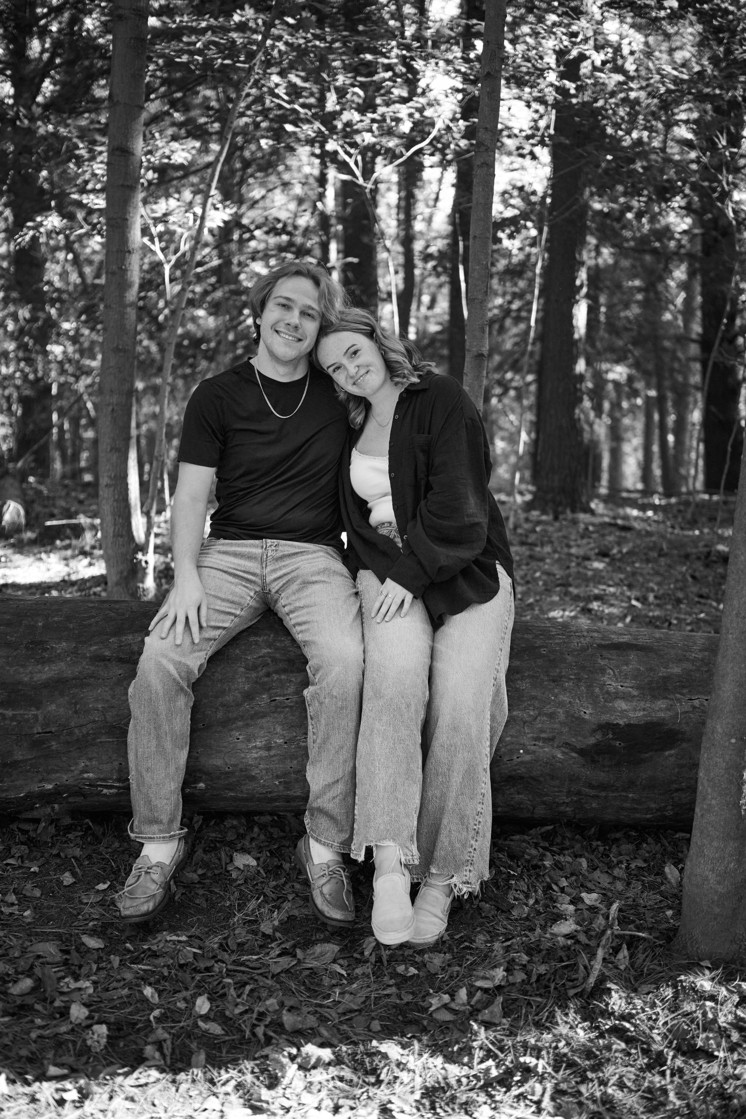 A couple sits together on a fallen log in a wooded forest setting, shown in three similar black and white photos.