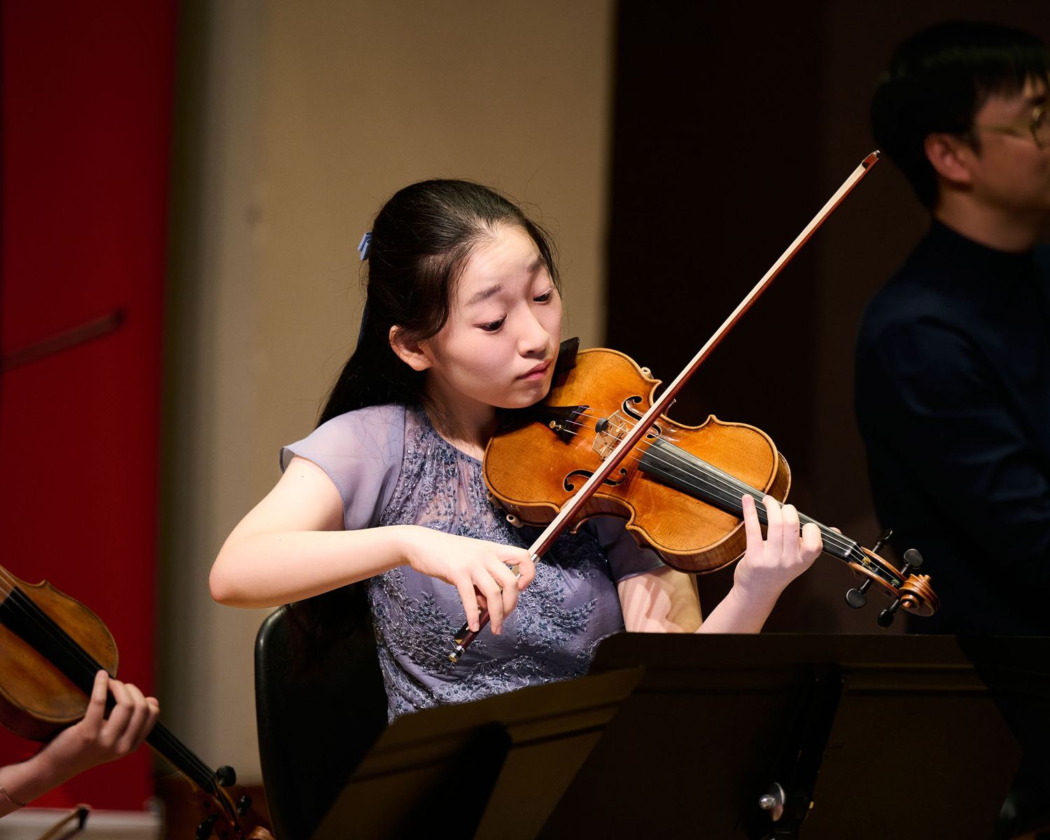 Young woman playing violin during a live orchestra performance on stage.