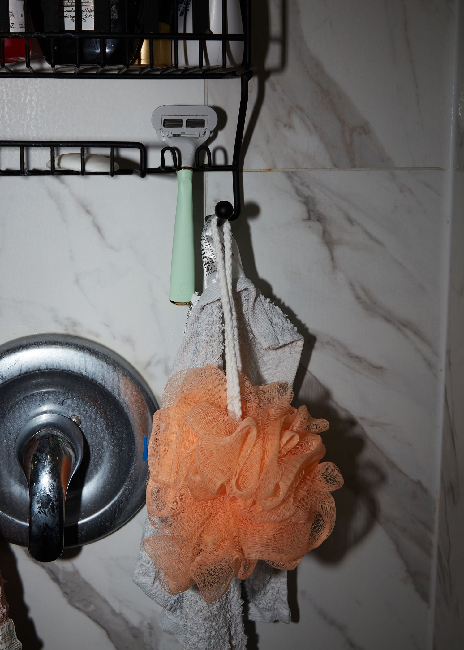 Orange loofah and mint green toiletries hanging on a marble-patterned bathroom wall.