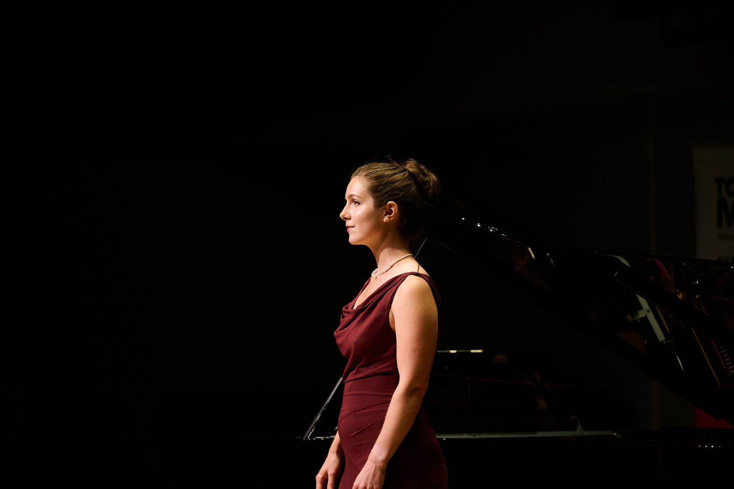 Woman in burgundy dress performing on stage under spotlight with microphone stand in dark background.