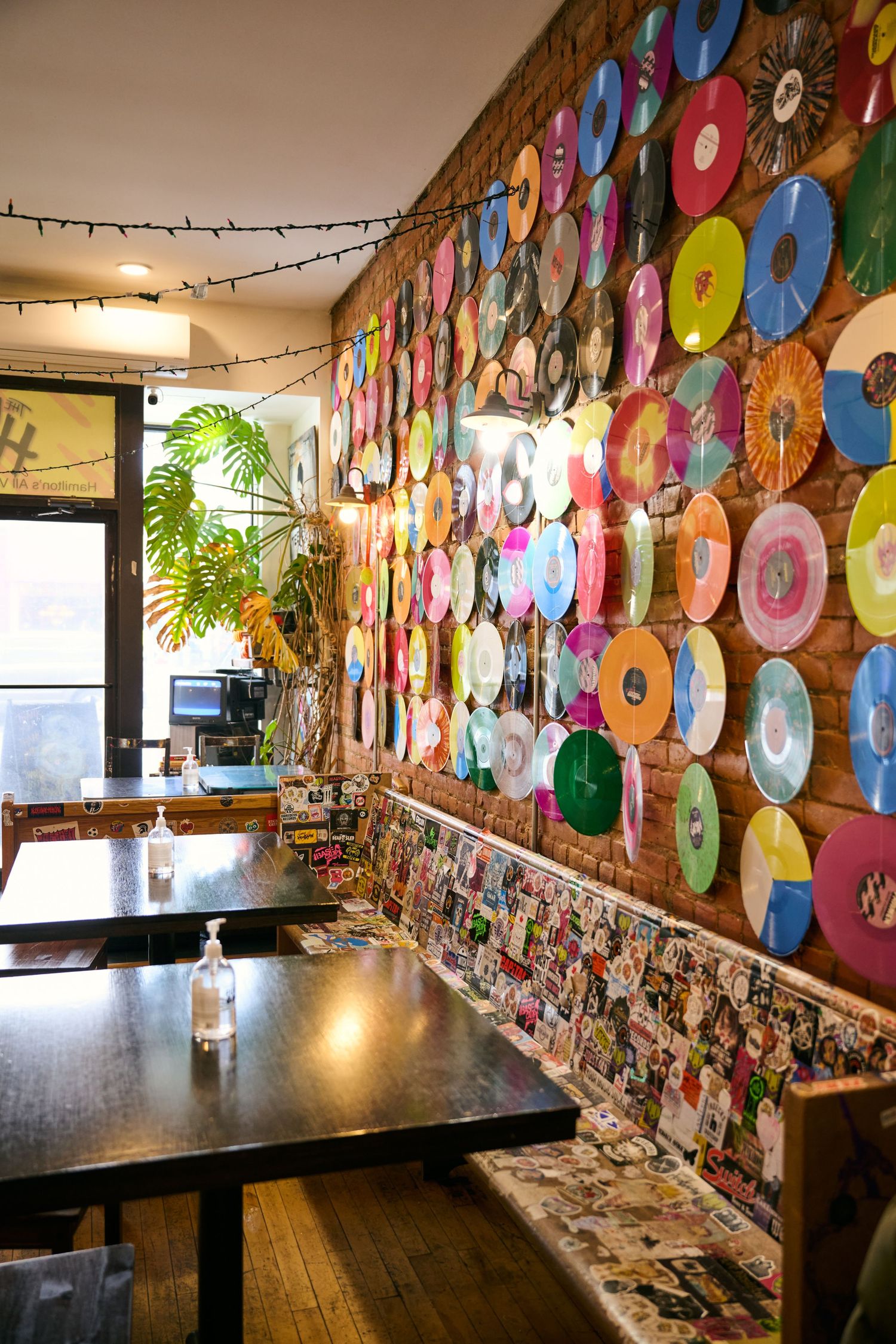 Eclectic restaurant interior decorated with colorful vinyl records on the wall and string lights overhead.