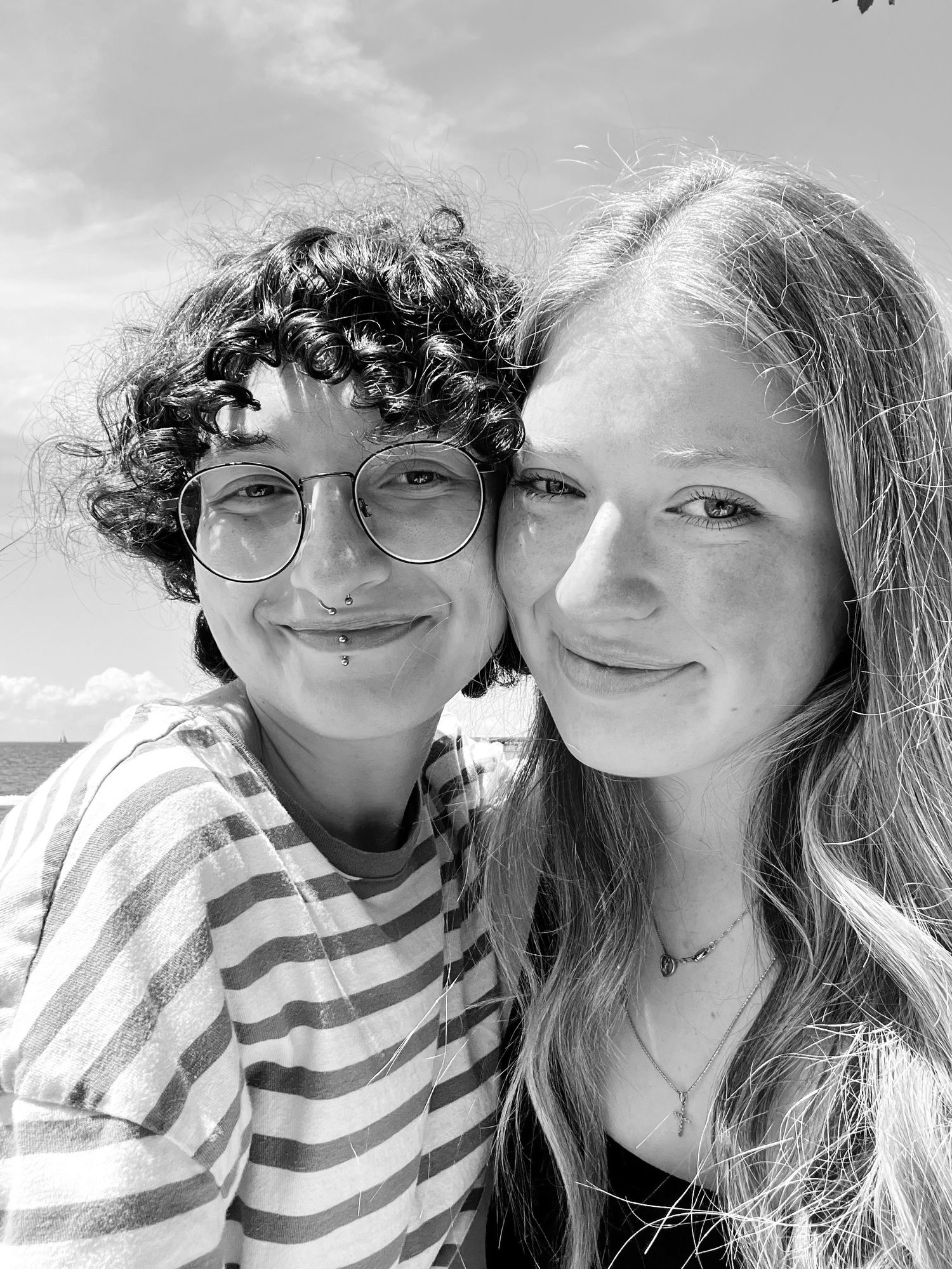 Black and white portrait of two friends smiling together outdoors on a sunny day.
