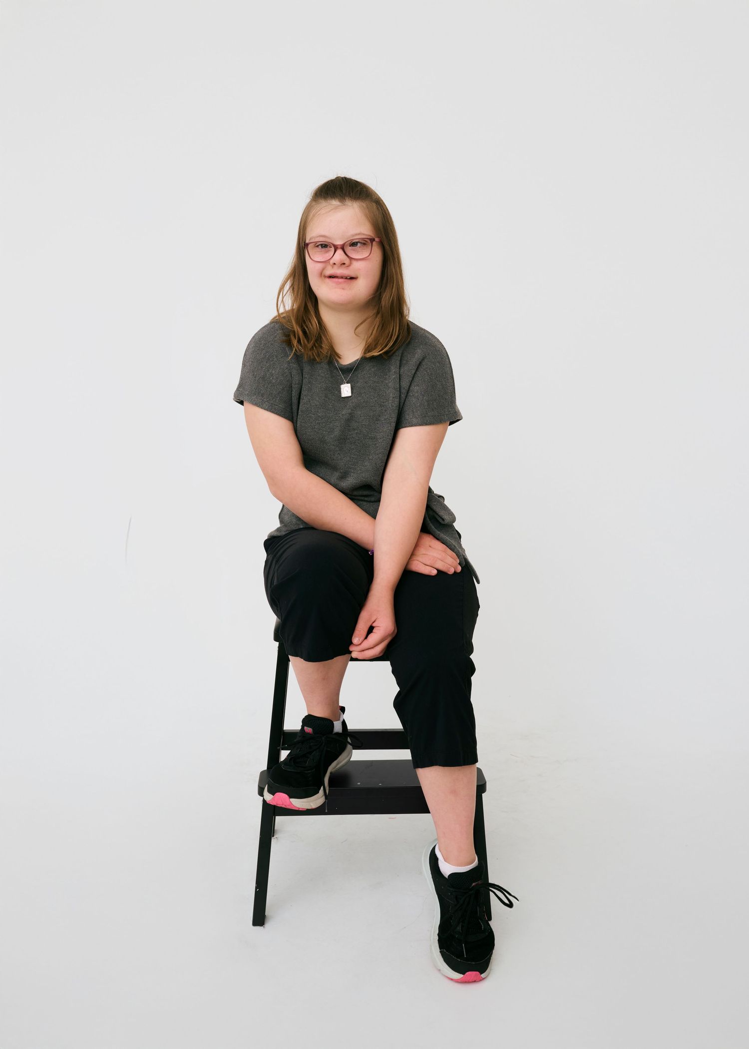 Four studio poses on a black stool wearing dark clothing against a white background.