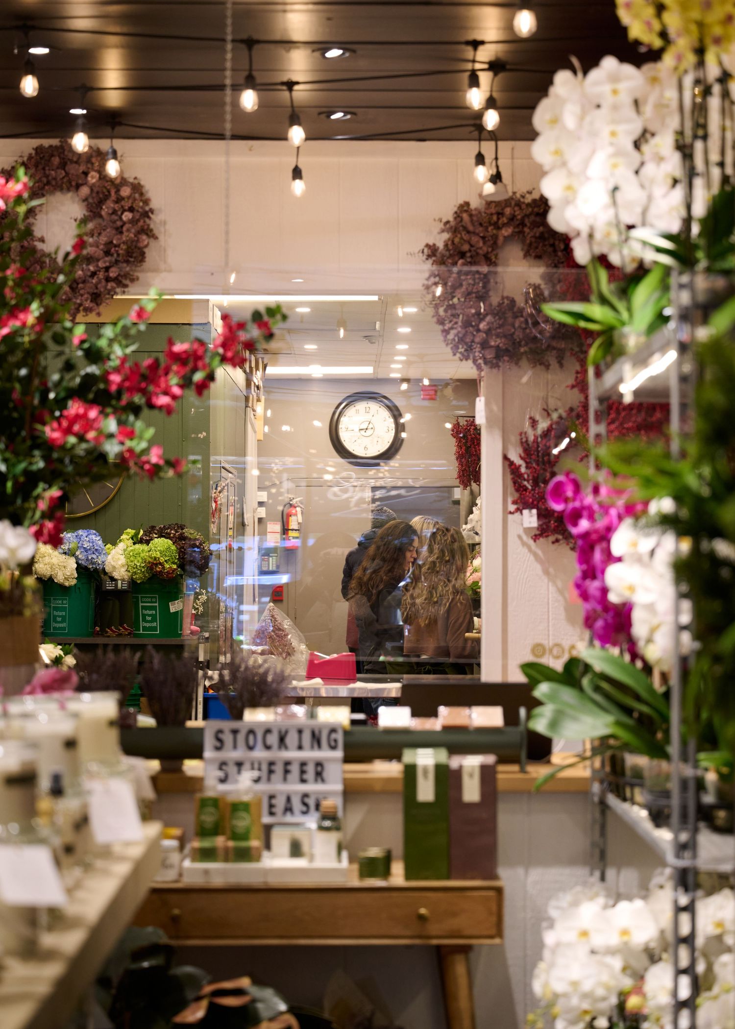 Rustic retail shop interior with hanging string lights, floral displays and stocking stuffer sign.