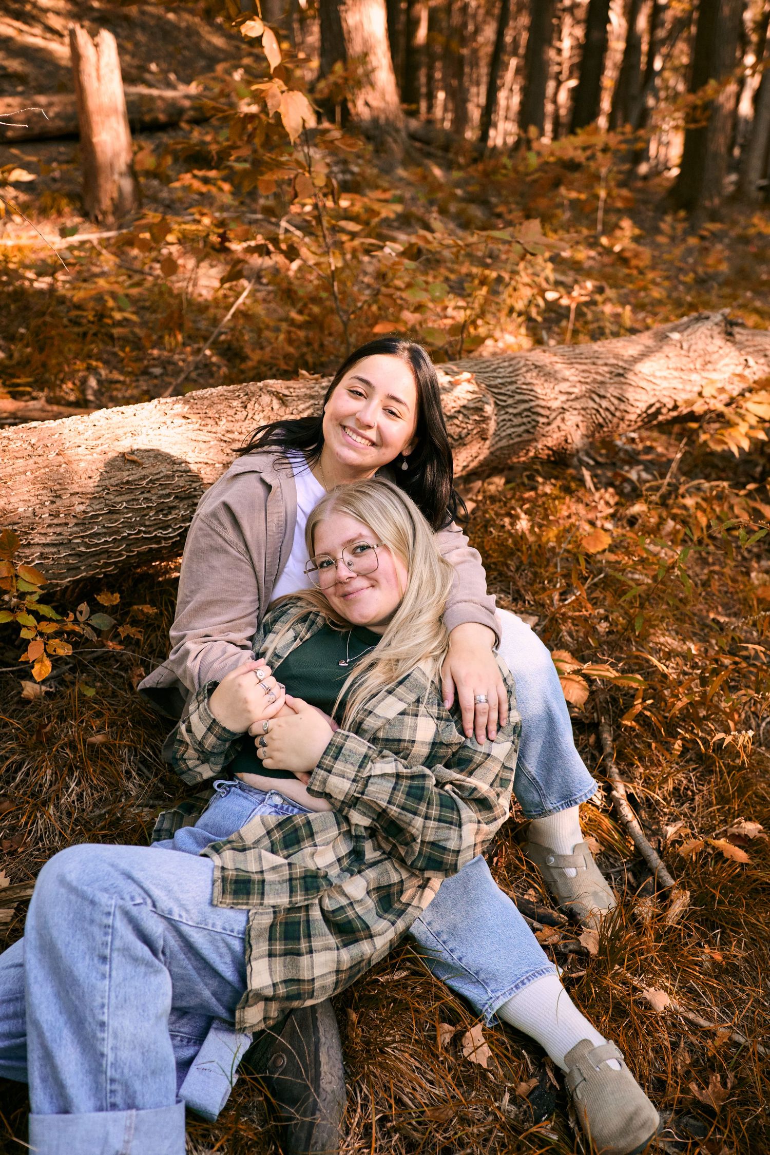 People relaxing together on fallen logs in an autumn forest with warm orange tones and dappled sunlight.