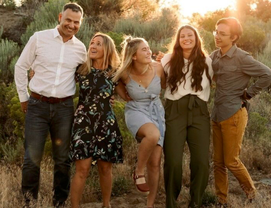 A group of people laughing and enjoying themselves while sitting outdoors during golden hour sunset.