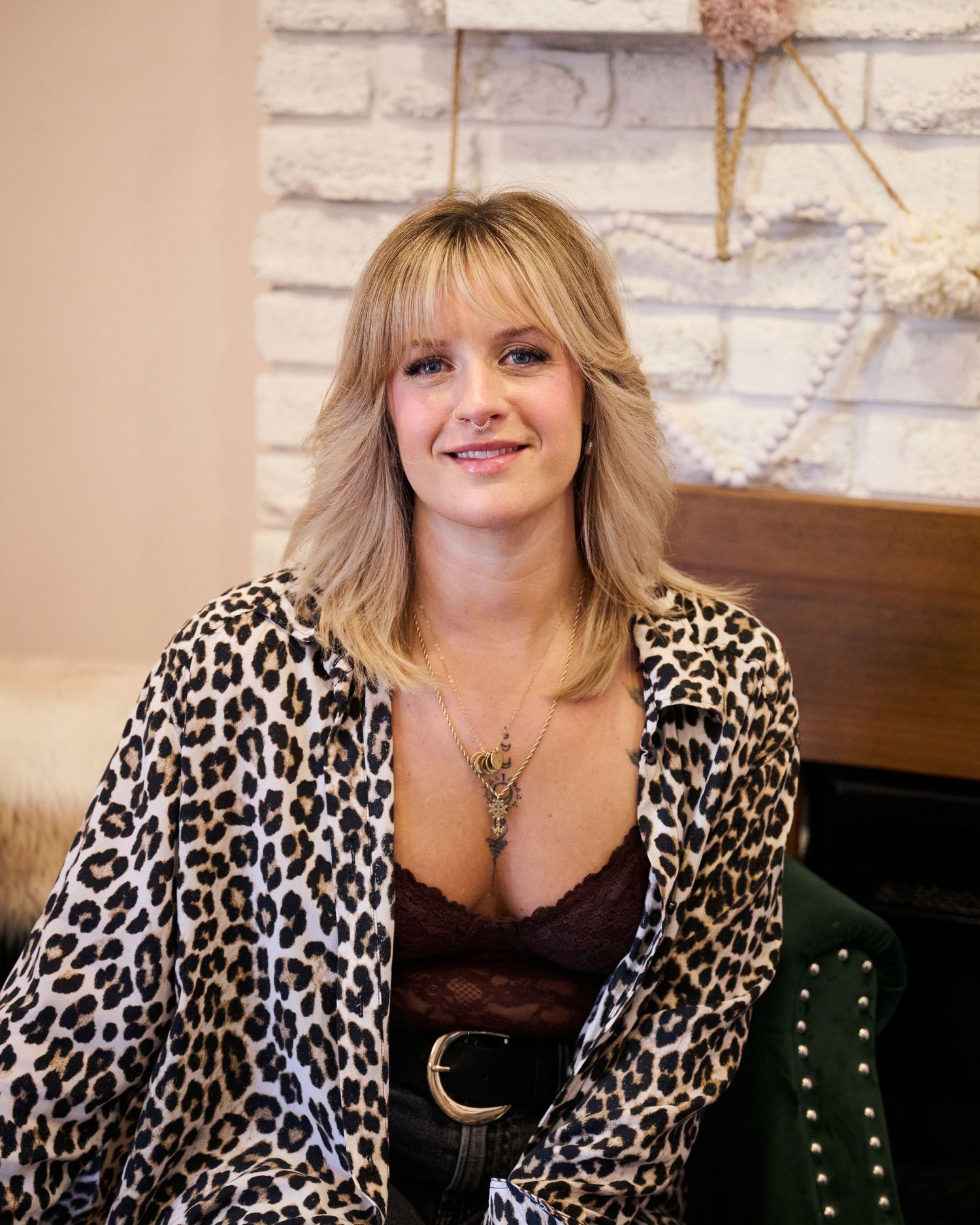 A person wearing a leopard print cardigan and black top poses against a white brick wall with decorative accents.