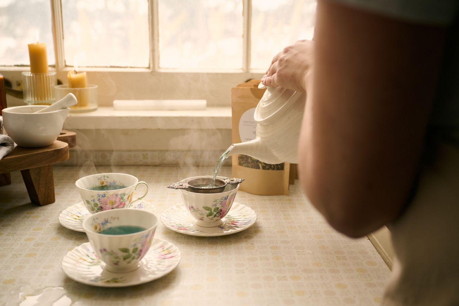 Vintage teacups and saucers arranged on table by window with soft natural lighting creating nostalgic mood.