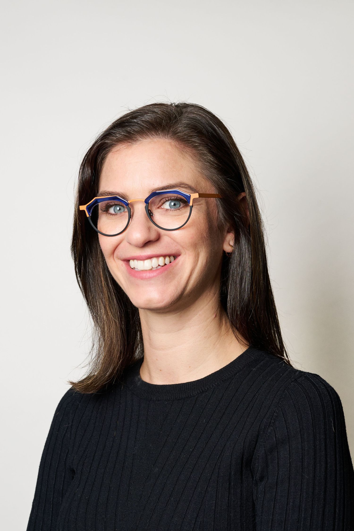 Studio portrait showing someone in black sweater and blue glasses against white background.