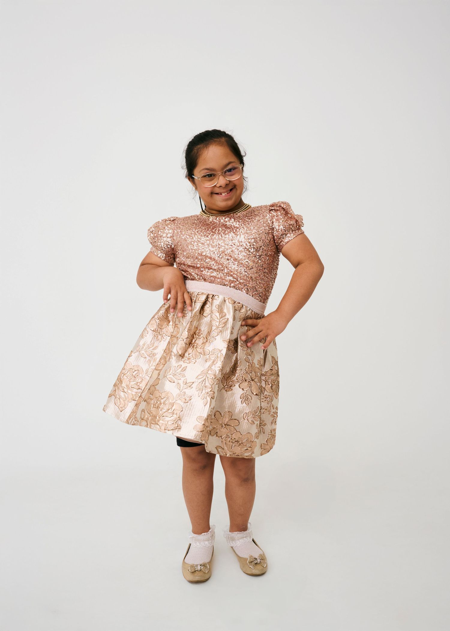 Person in rose gold sequin dress and flats poses cheerfully against white background.