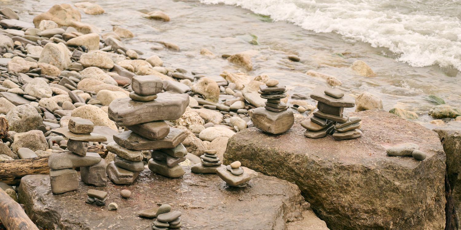 Multiple stacks of balanced stones create artistic cairns along a rocky coastal shoreline in nature.
