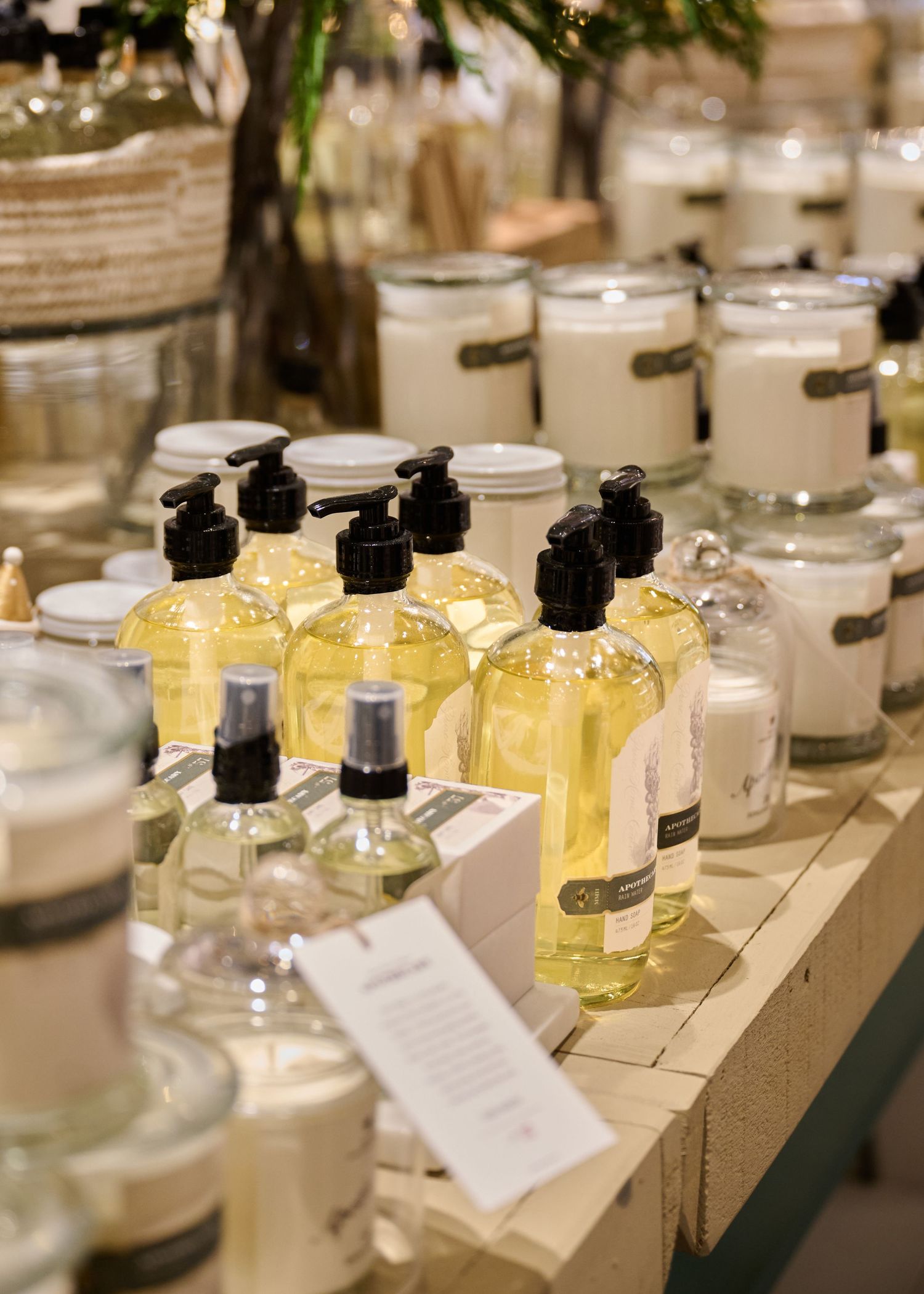 Glass jars of lotions, soaps and candles displayed on a wooden table at a boutique store or spa setting.