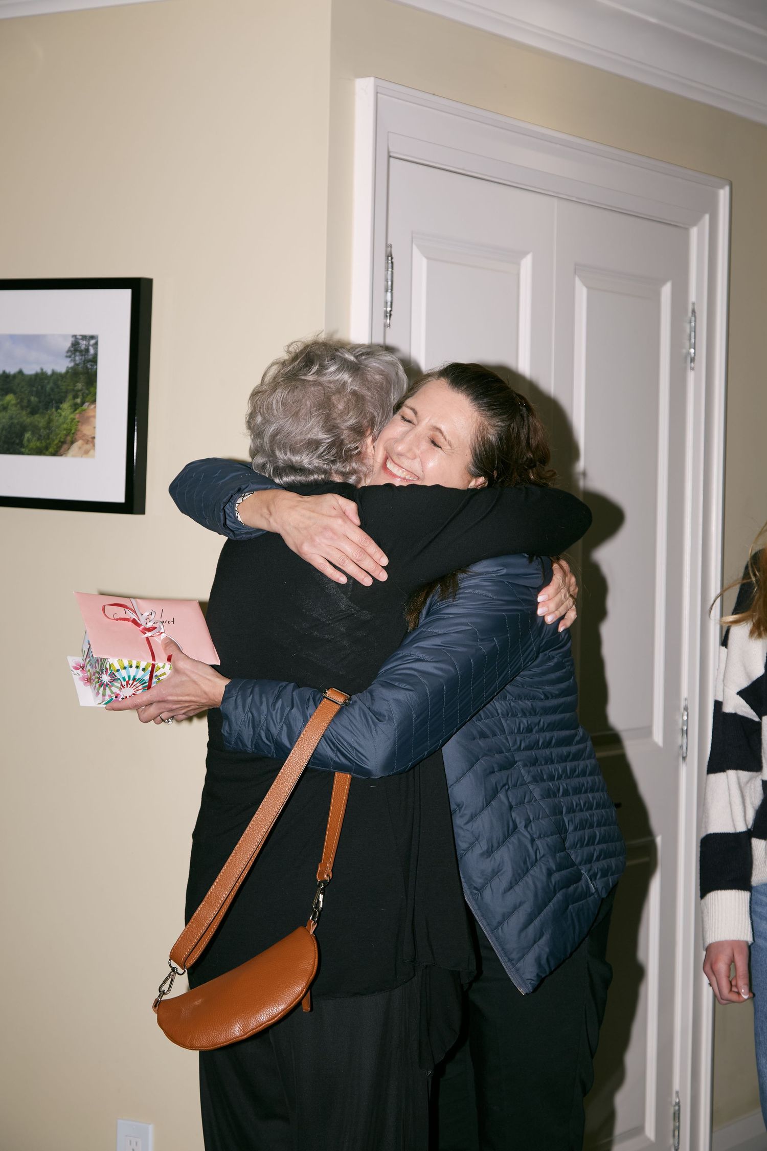 Two people sharing a warm embrace in a hallway with white walls and doors.