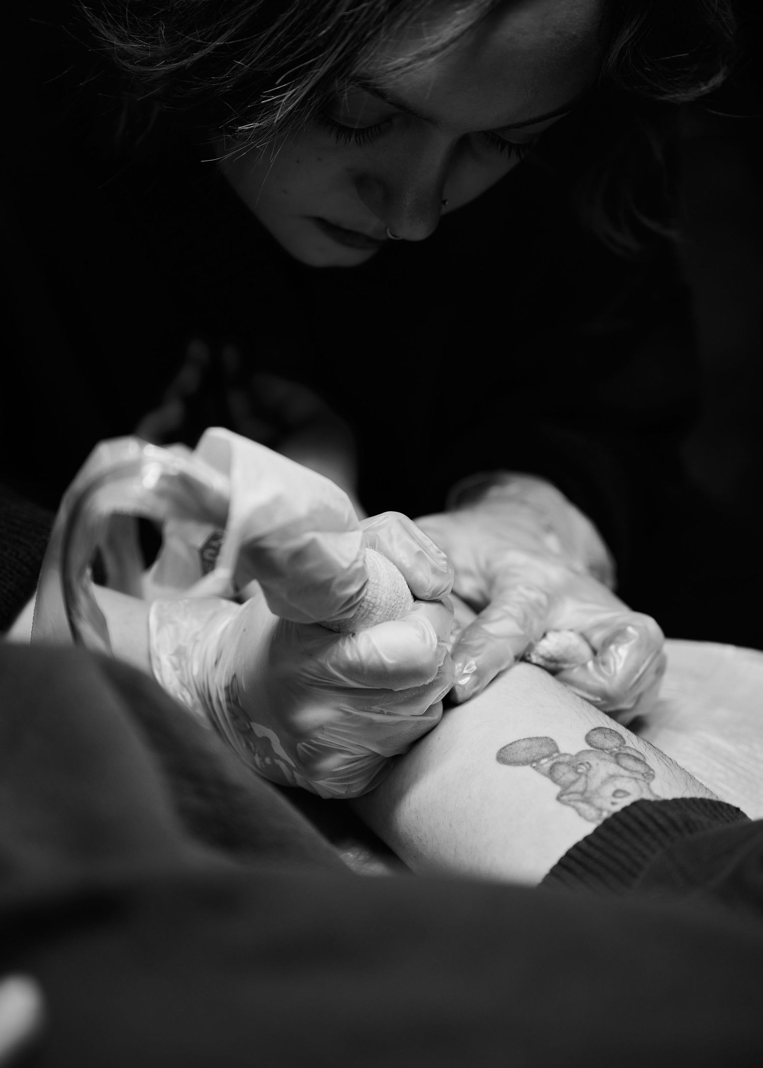 Close-up black and white image of hands working on a tattoo.