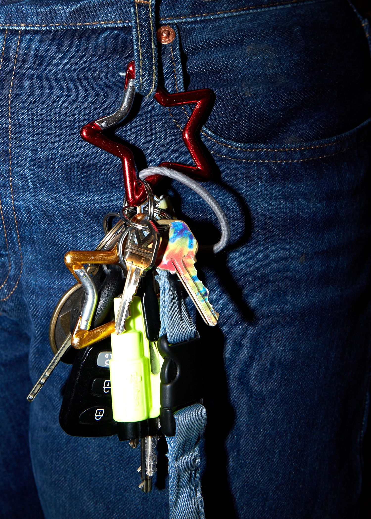 Keys attached to a red star-shaped keychain hanging on denim jeans pocket.
