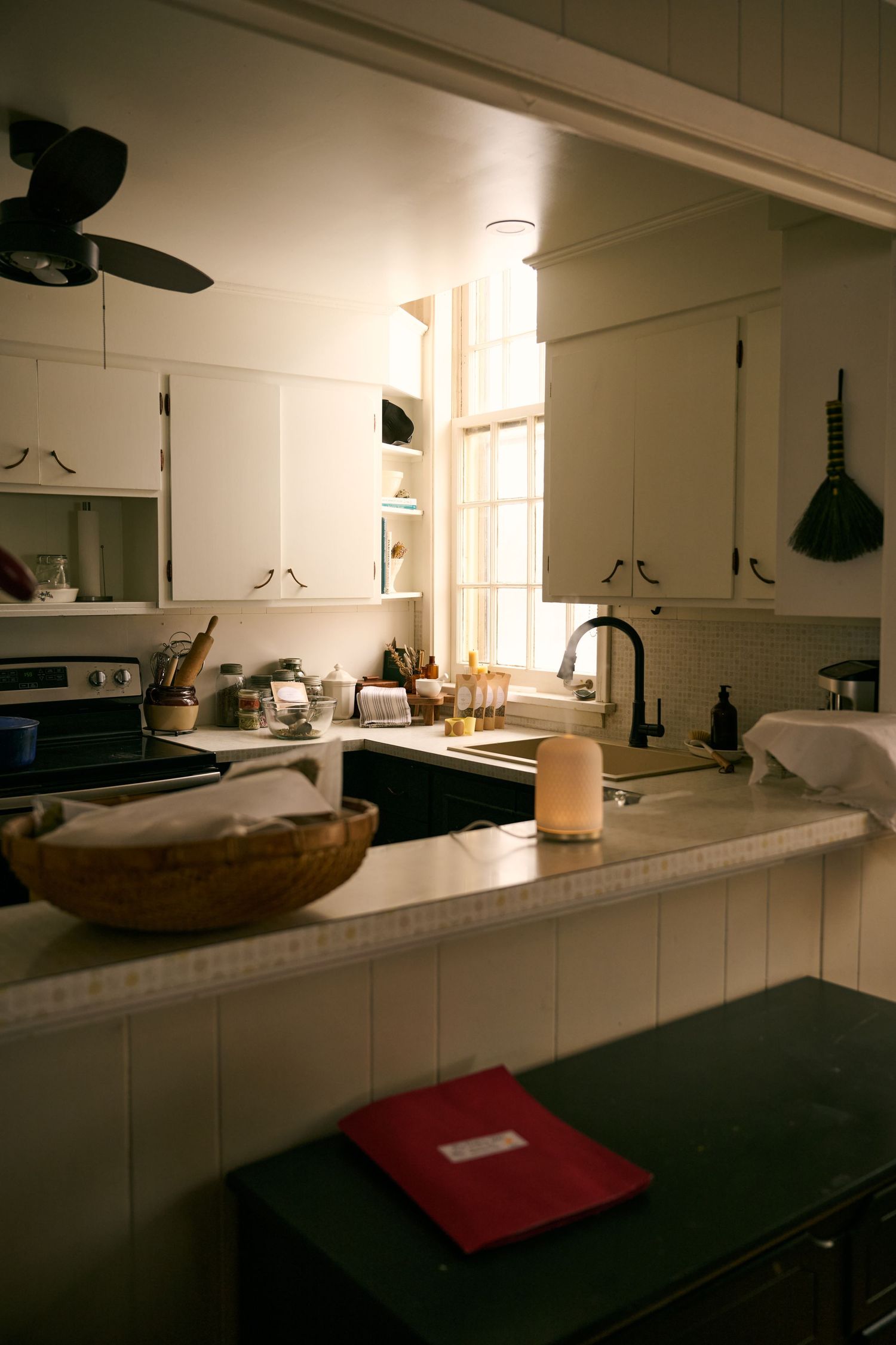 A cozy vintage kitchen with white cabinets, wooden bowl, and warm lighting filtering through a window.