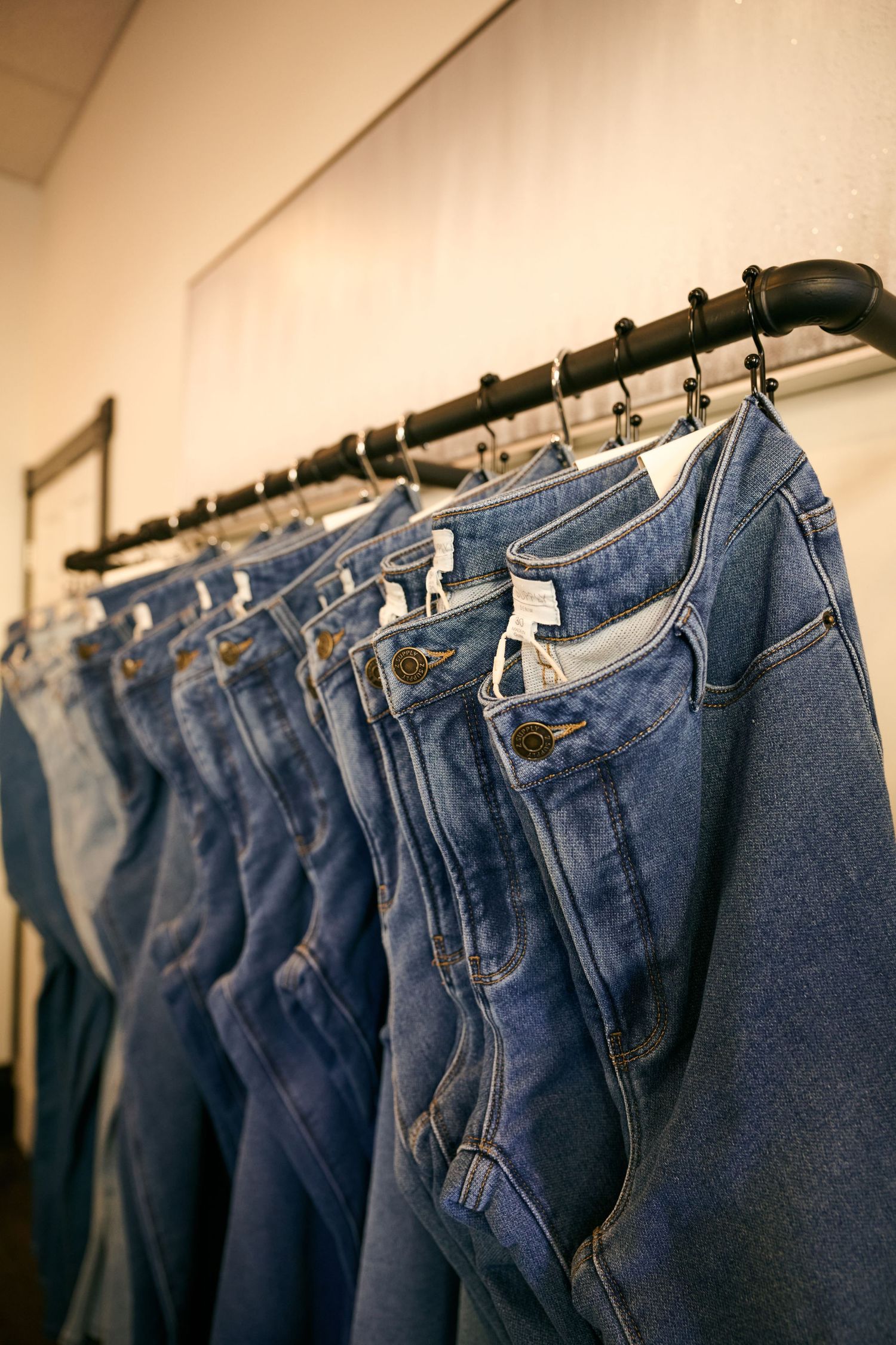 A row of blue denim jeans hanging on black metal hangers displayed on a retail clothing rack.