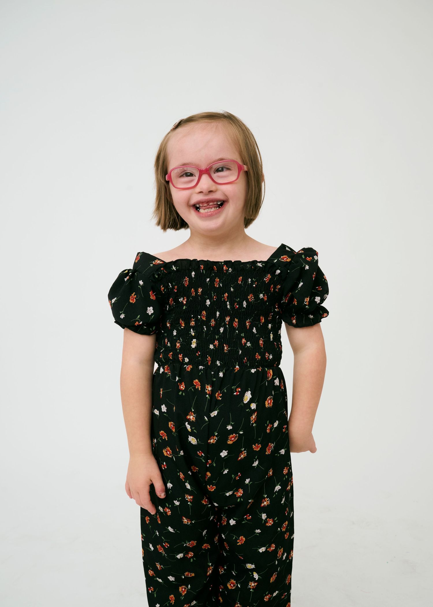 A model wearing a black floral dress poses playfully against a white background.