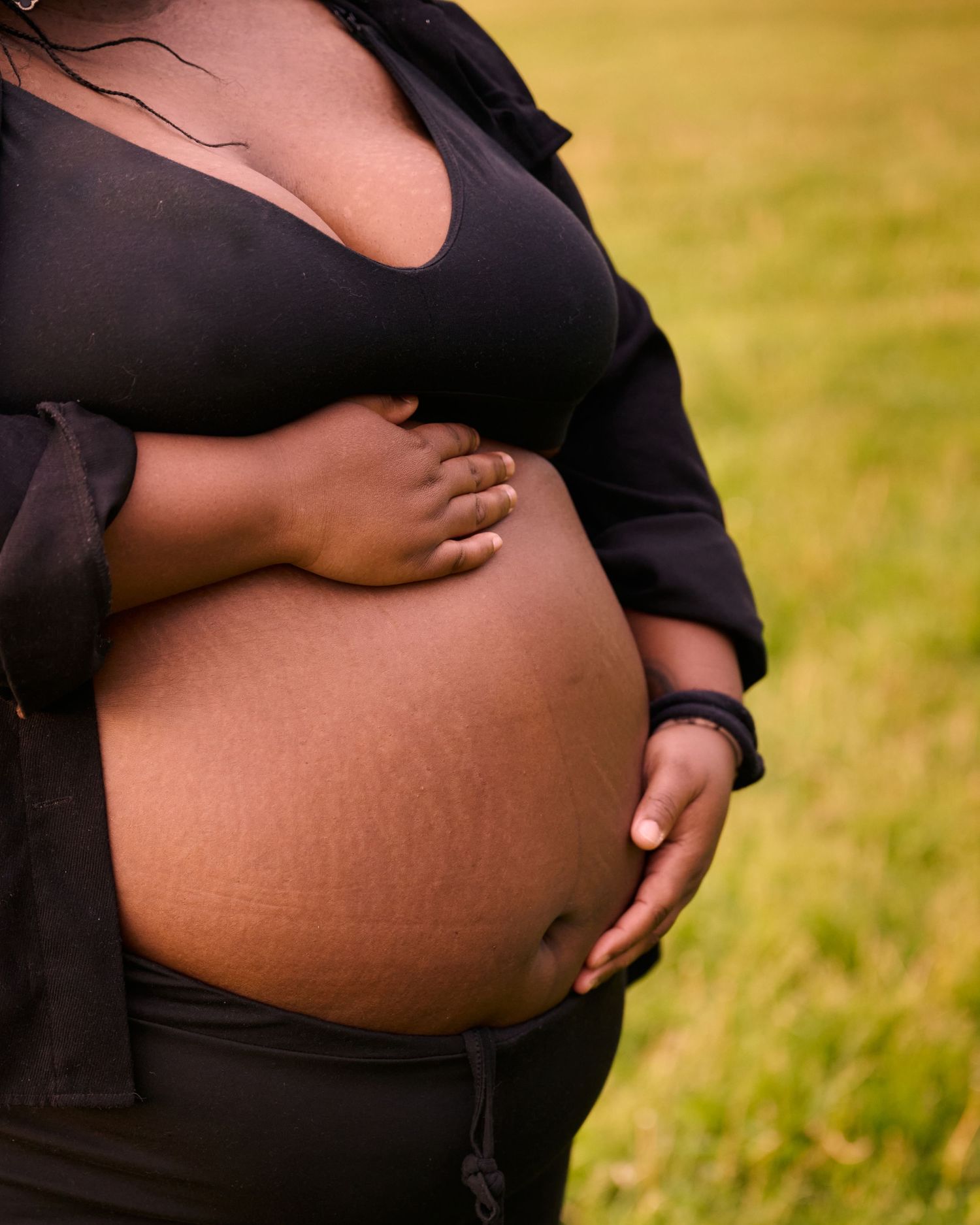 Close-up view of a pregnant belly in black clothing against a blurred outdoor background.