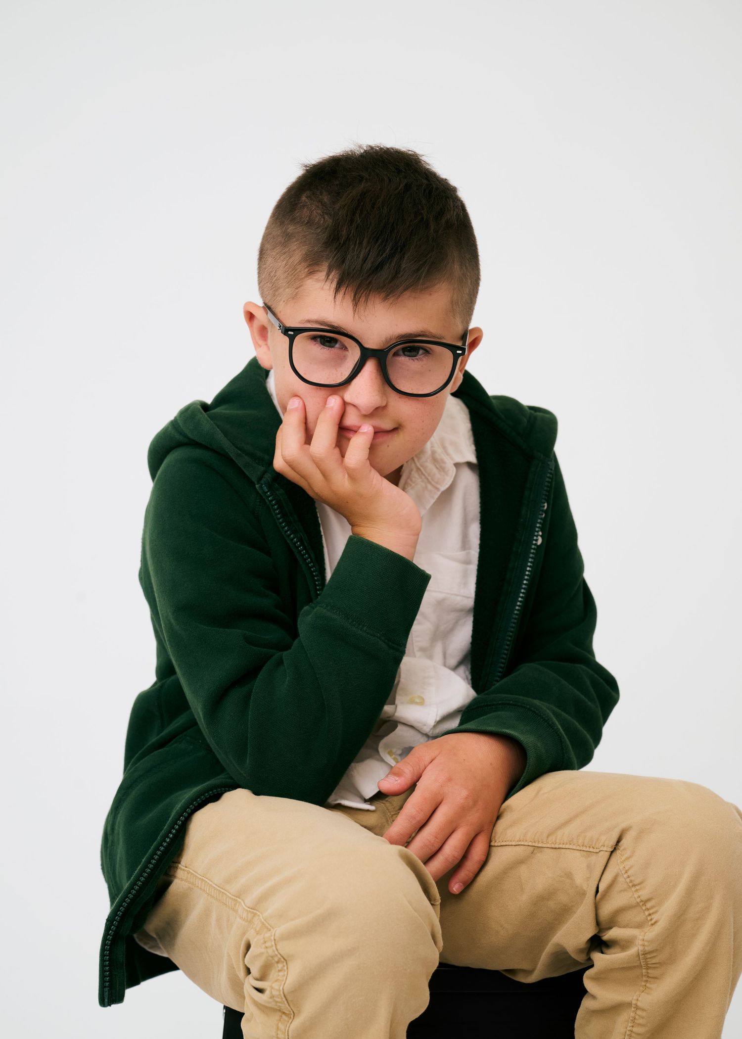 Person in dark blazer and khaki pants sits casually while showing various expressions.