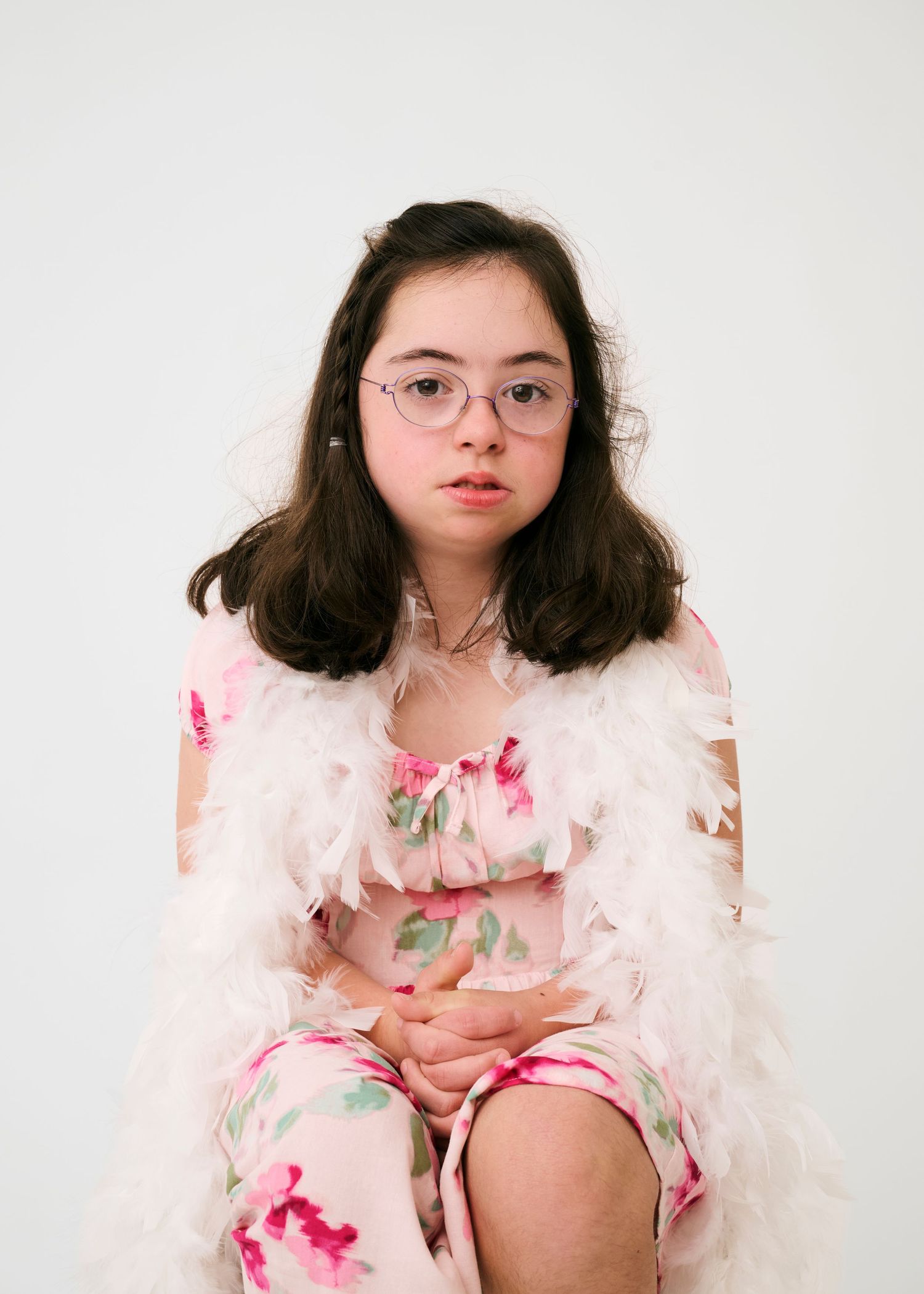Person wearing round glasses and a pink floral dress with feather details poses against a white background.