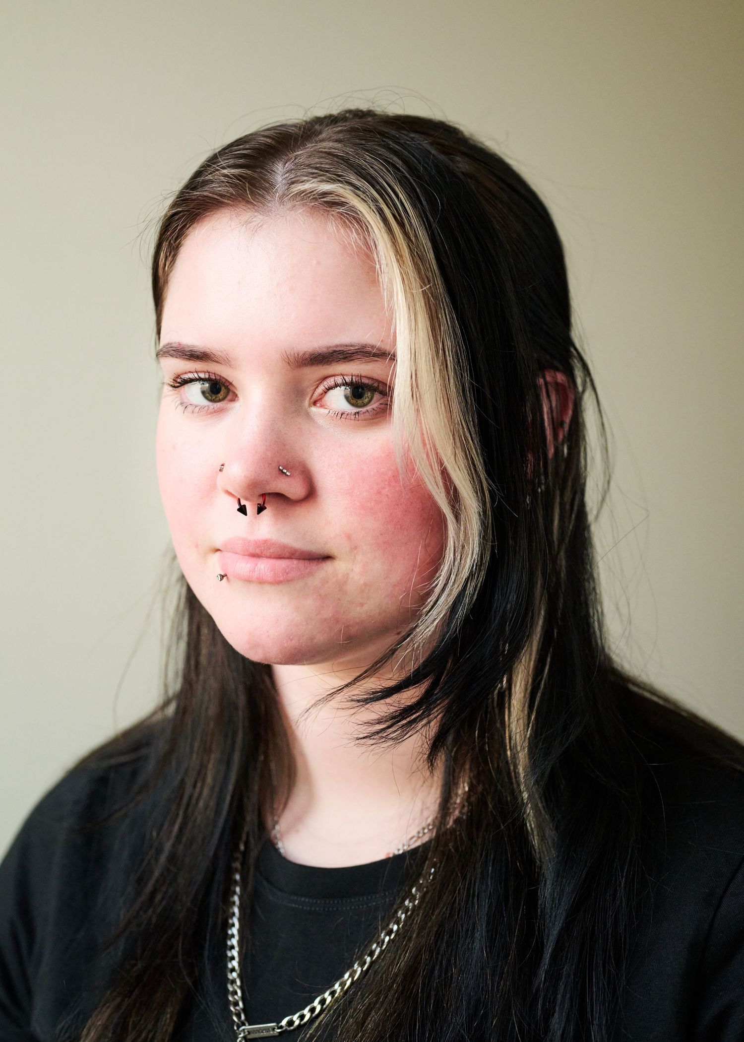 A person with black and blonde two-toned hair wearing a black top poses against a plain wall in a photo sequence.