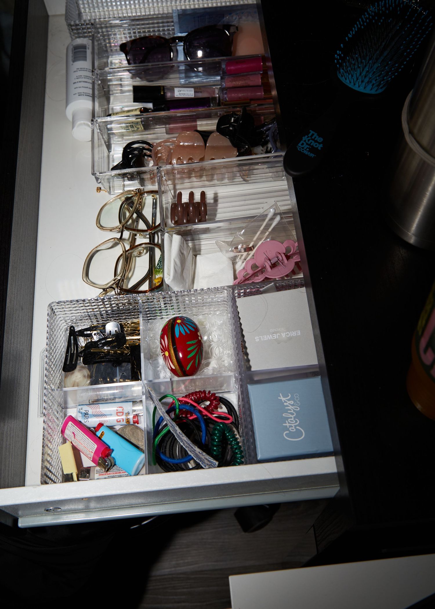 An organized drawer containing glasses, accessories and personal items neatly arranged in compartments.