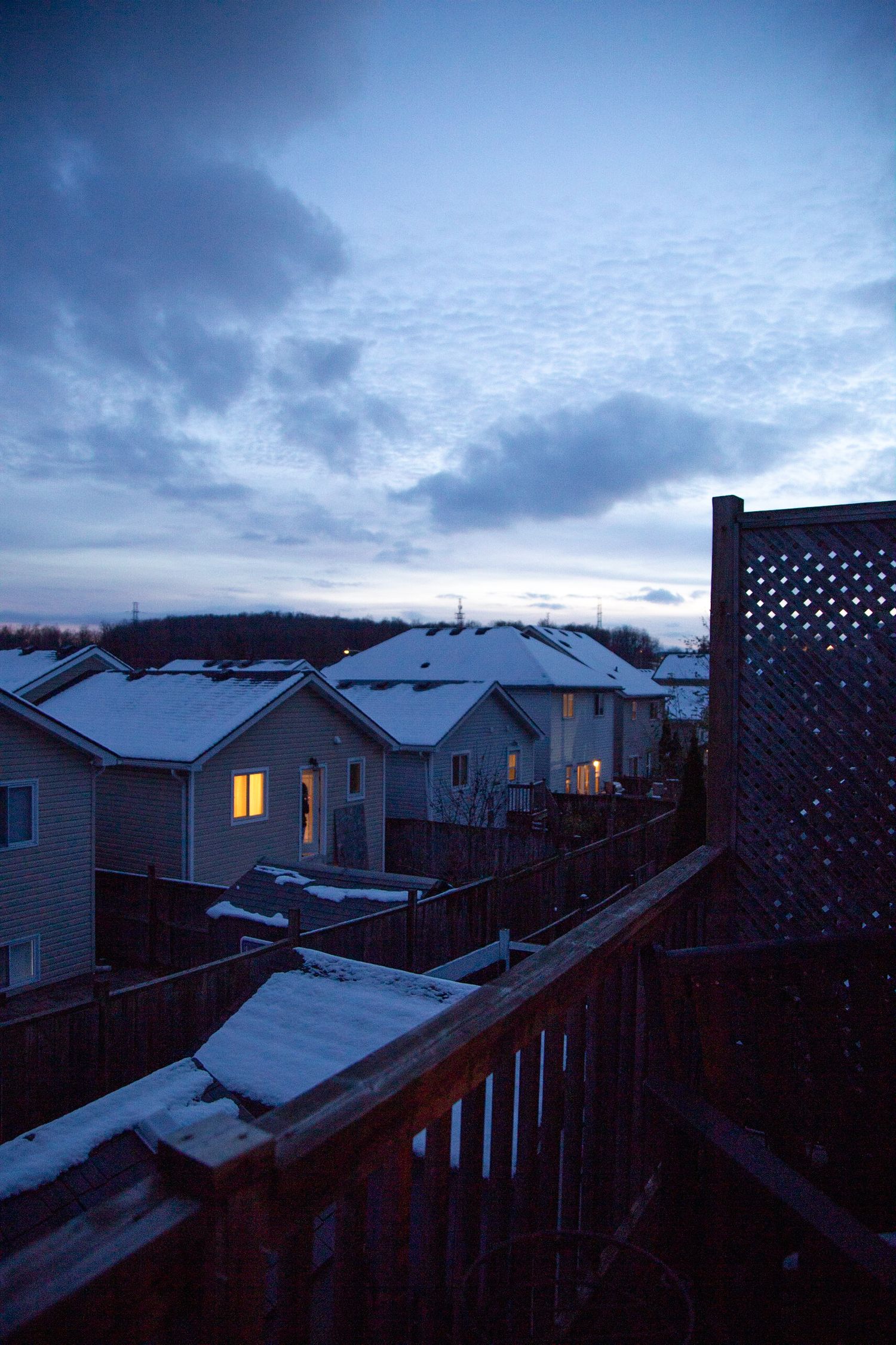 Snowy rooftops of suburban homes at twilight with dark blue sky and clouds overhead.