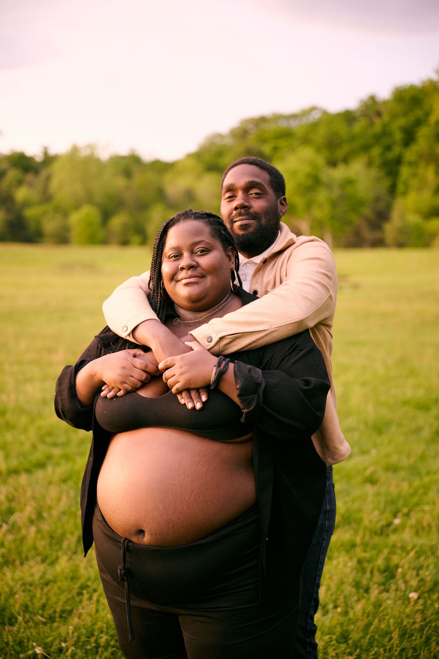 A couple embraces lovingly in a sunlit meadow during a maternity photoshoot.