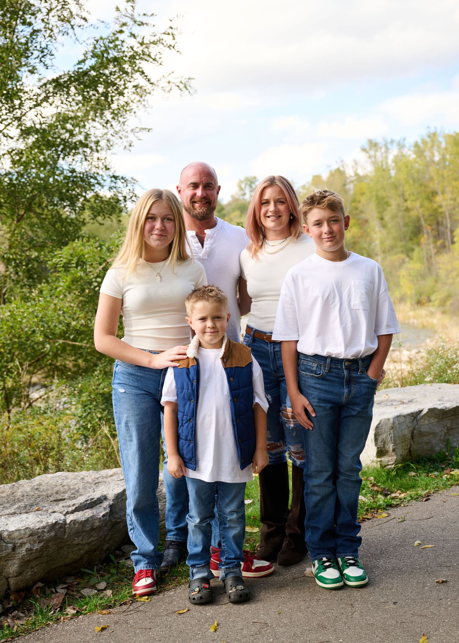 A group stands together on a stone path outdoors during autumn with trees and foliage visible in the background.