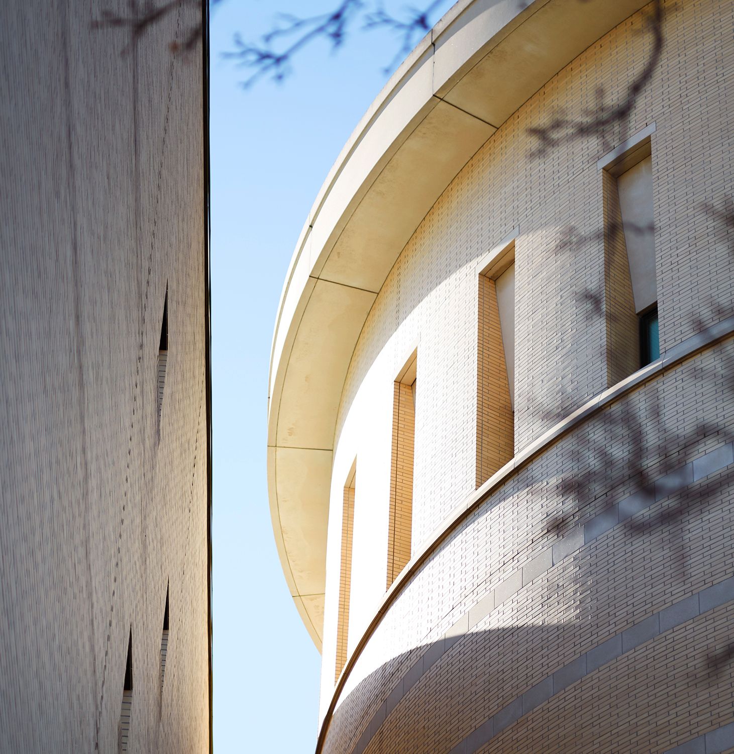 Modern curved white building facade with arched details against bright blue sky.