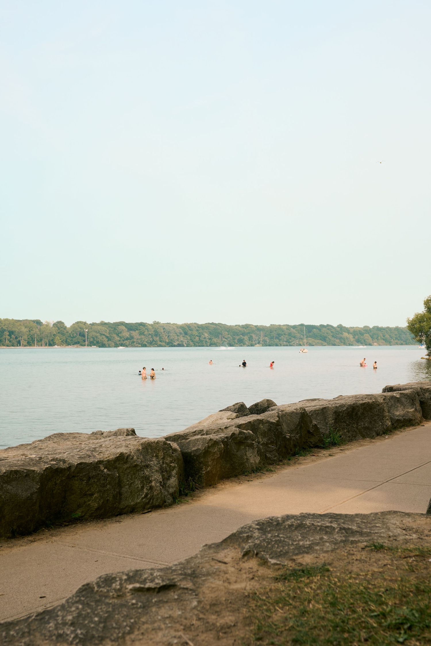 A panoramic view of a beach shoreline with rocky outcrops along a sandy path and distant treeline on the horizon.