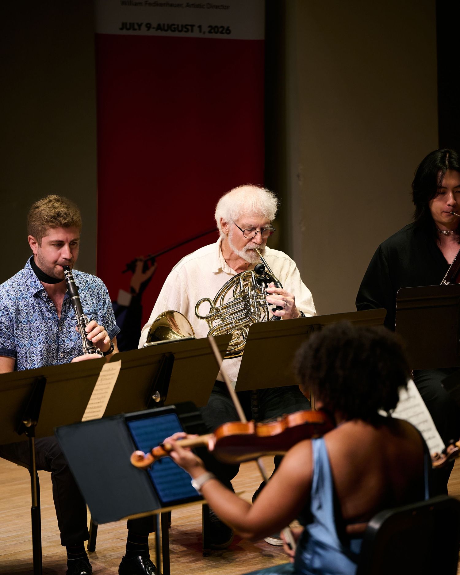 Musicians perform chamber music, featuring clarinet, French horn, and violin players at a summer orchestra program.