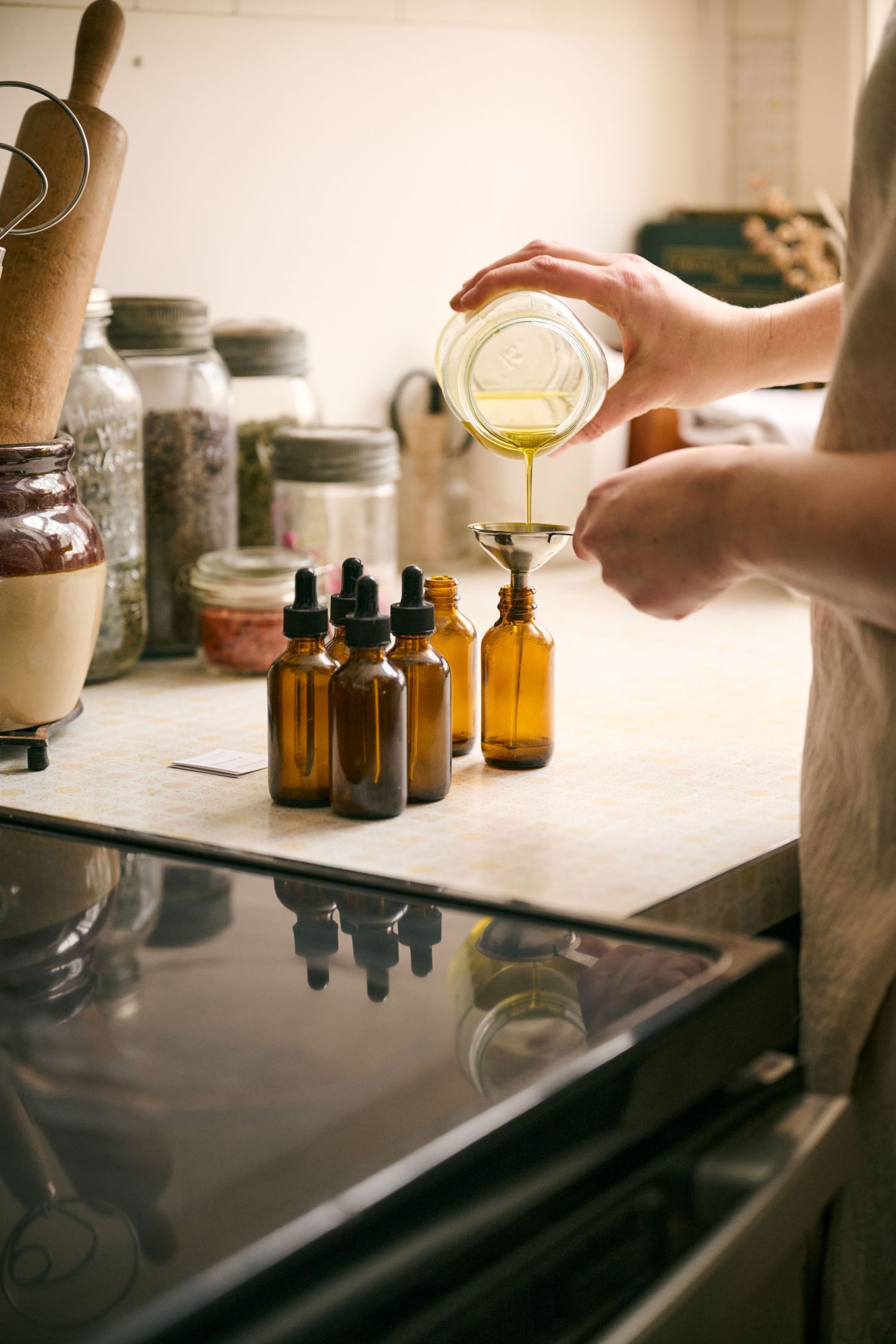 Hands pouring essential oils into amber bottles on a kitchen counter.