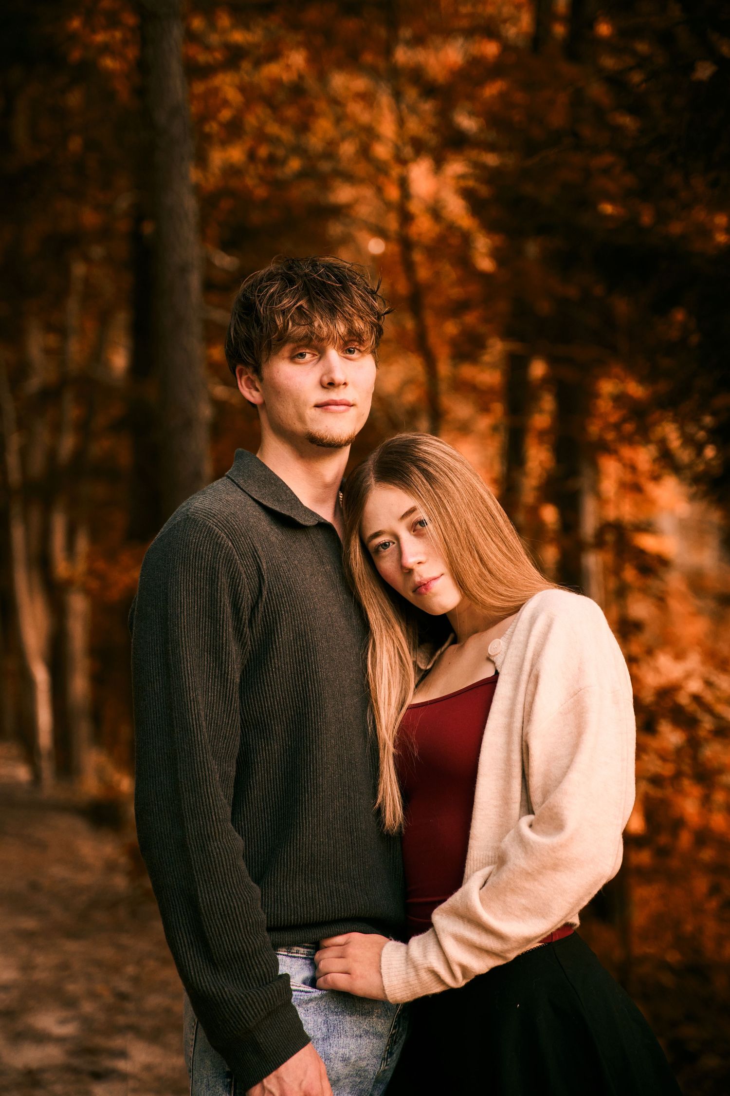 A romantic autumn photo shoot in a forest with warm orange foliage in the background.