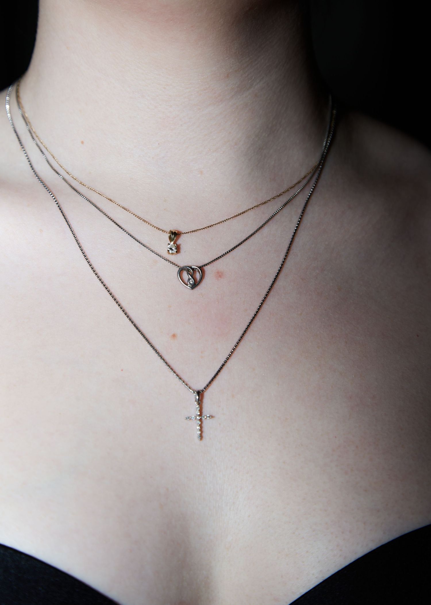 A layered silver necklace with three delicate chains featuring heart and cross pendants.