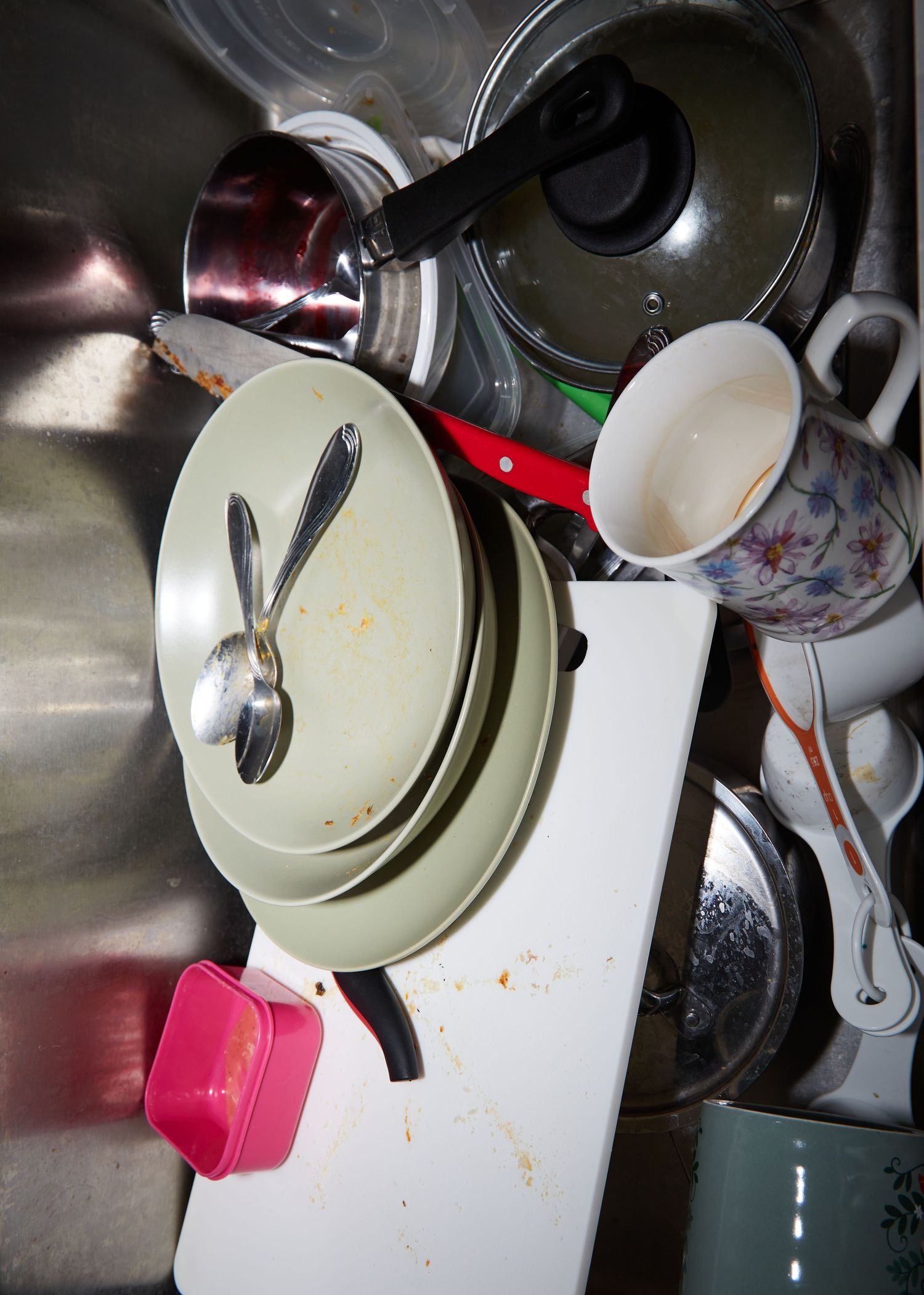 Kitchen items including plates and utensils stacked in a stainless steel sink.