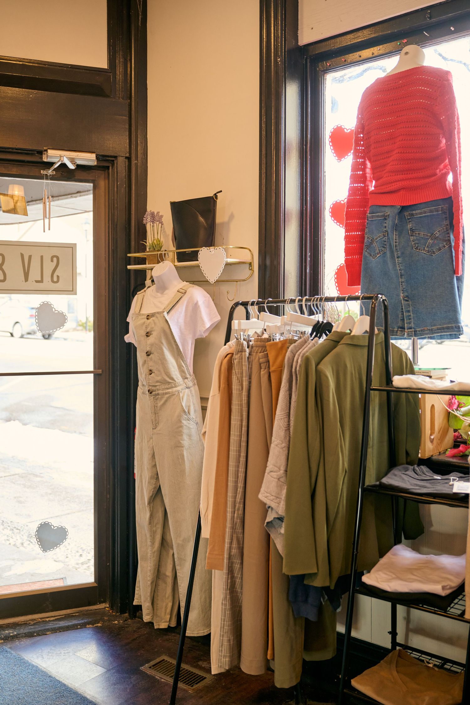 Clothing display in a boutique showing casual apparel with coats and jeans on racks near sunlit windows.