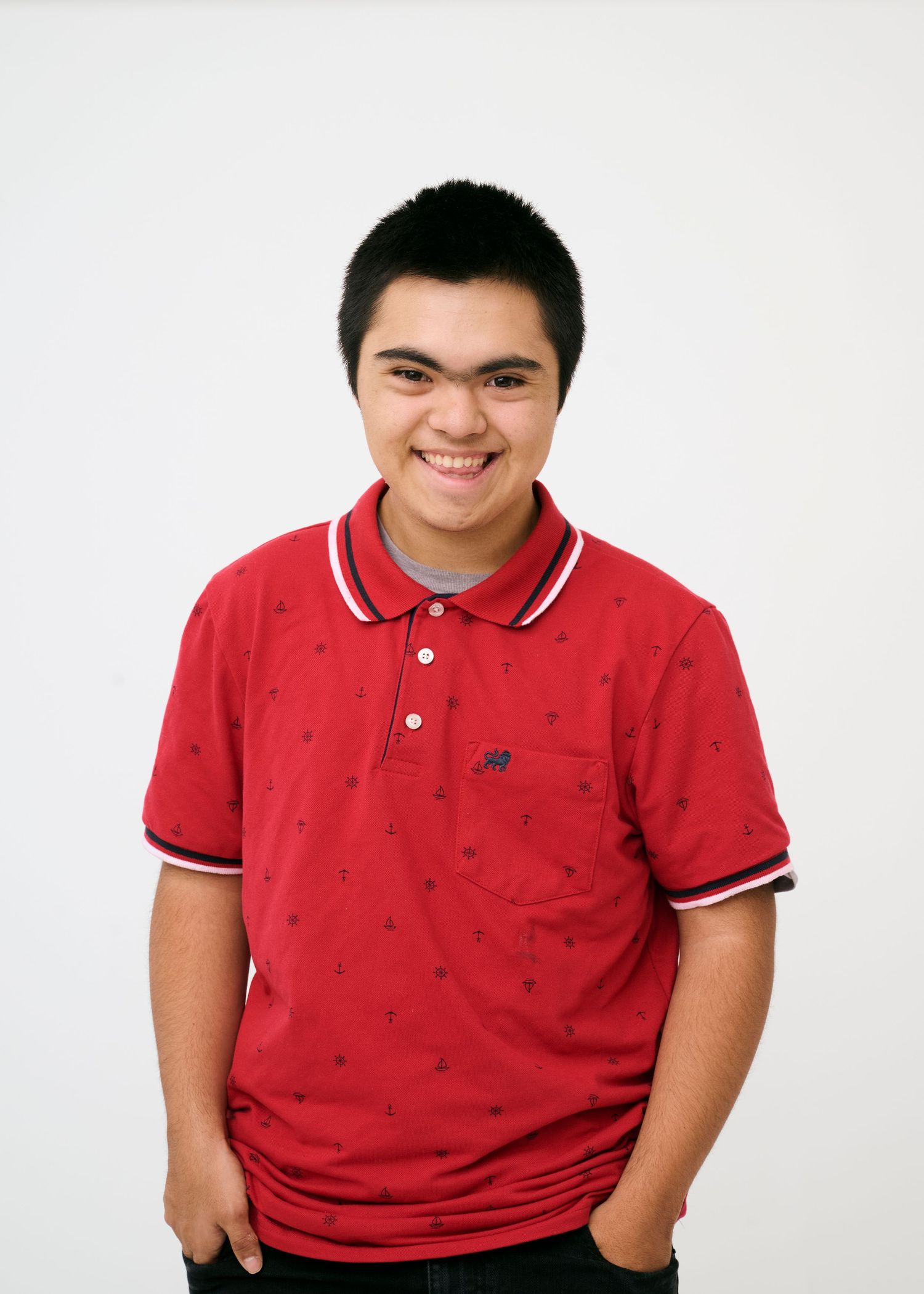 Person in red polo shirt with pattern smiles warmly against white studio backdrop.