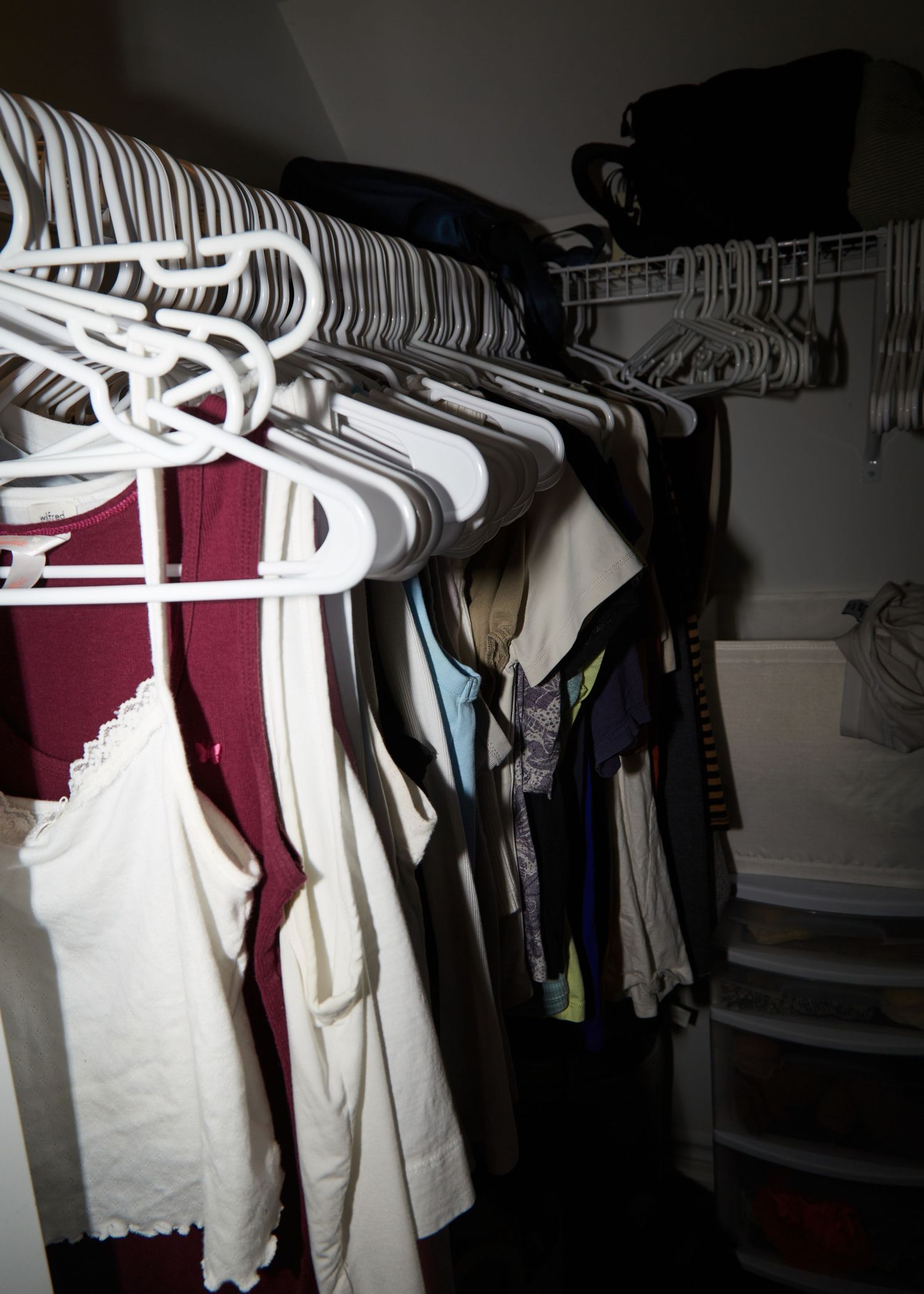 Organized closet with white hangers holding various clothing items.