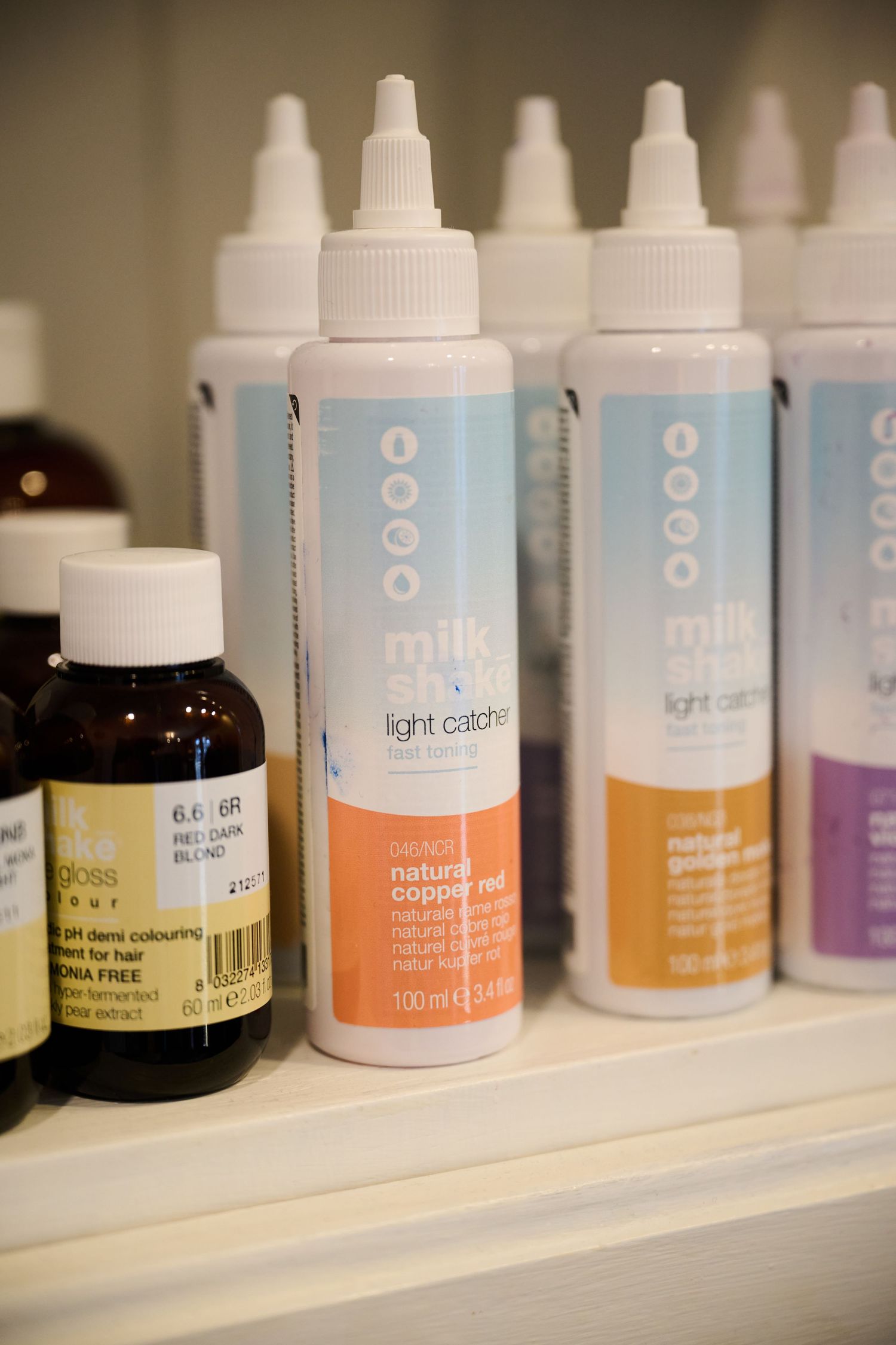 Close-up of milk_shake professional hair care product bottles with orange and blue labels on a shelf.