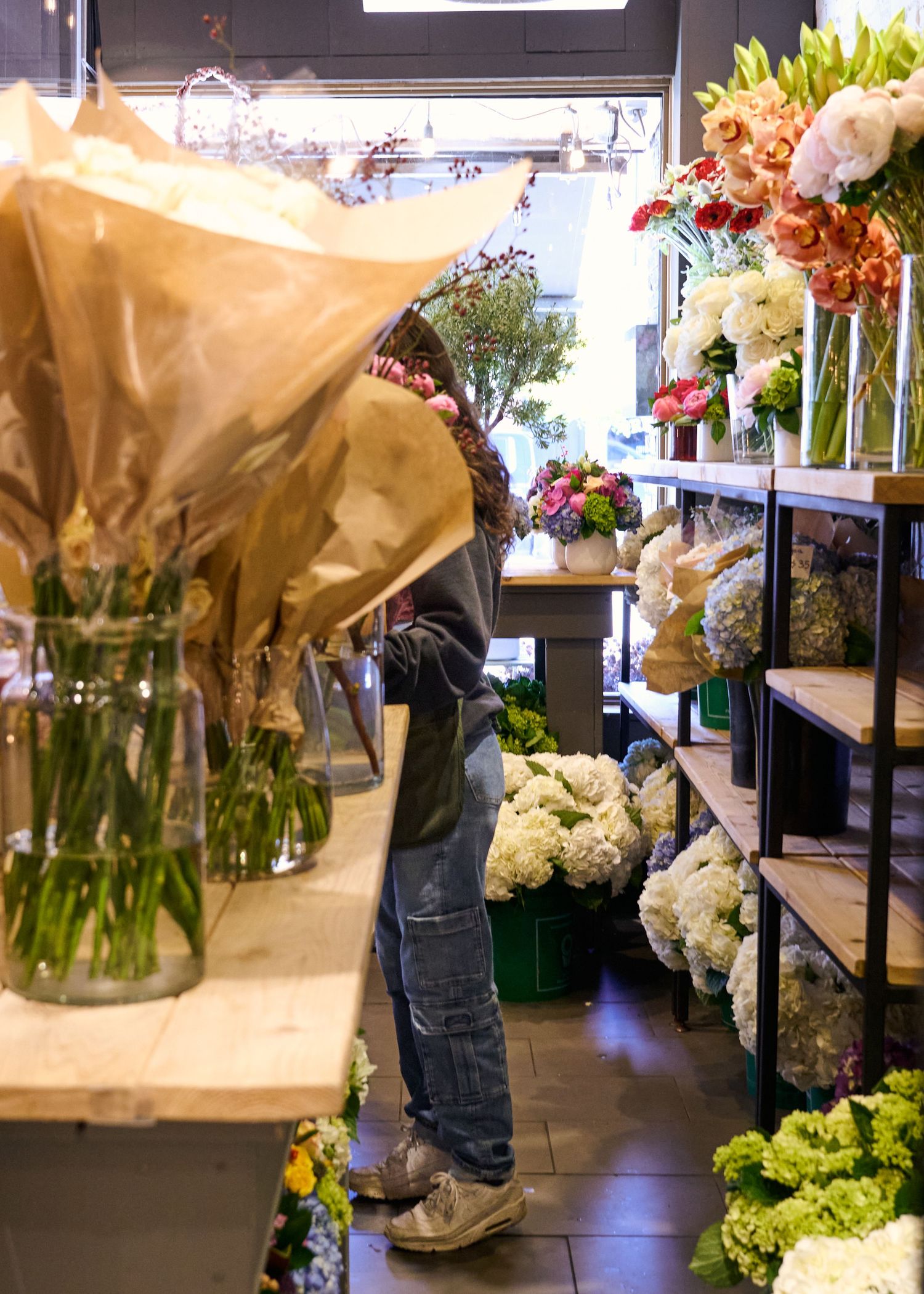Inside a flower shop with wrapped bouquets, shelving displays, and hydrangeas visible on the floor.