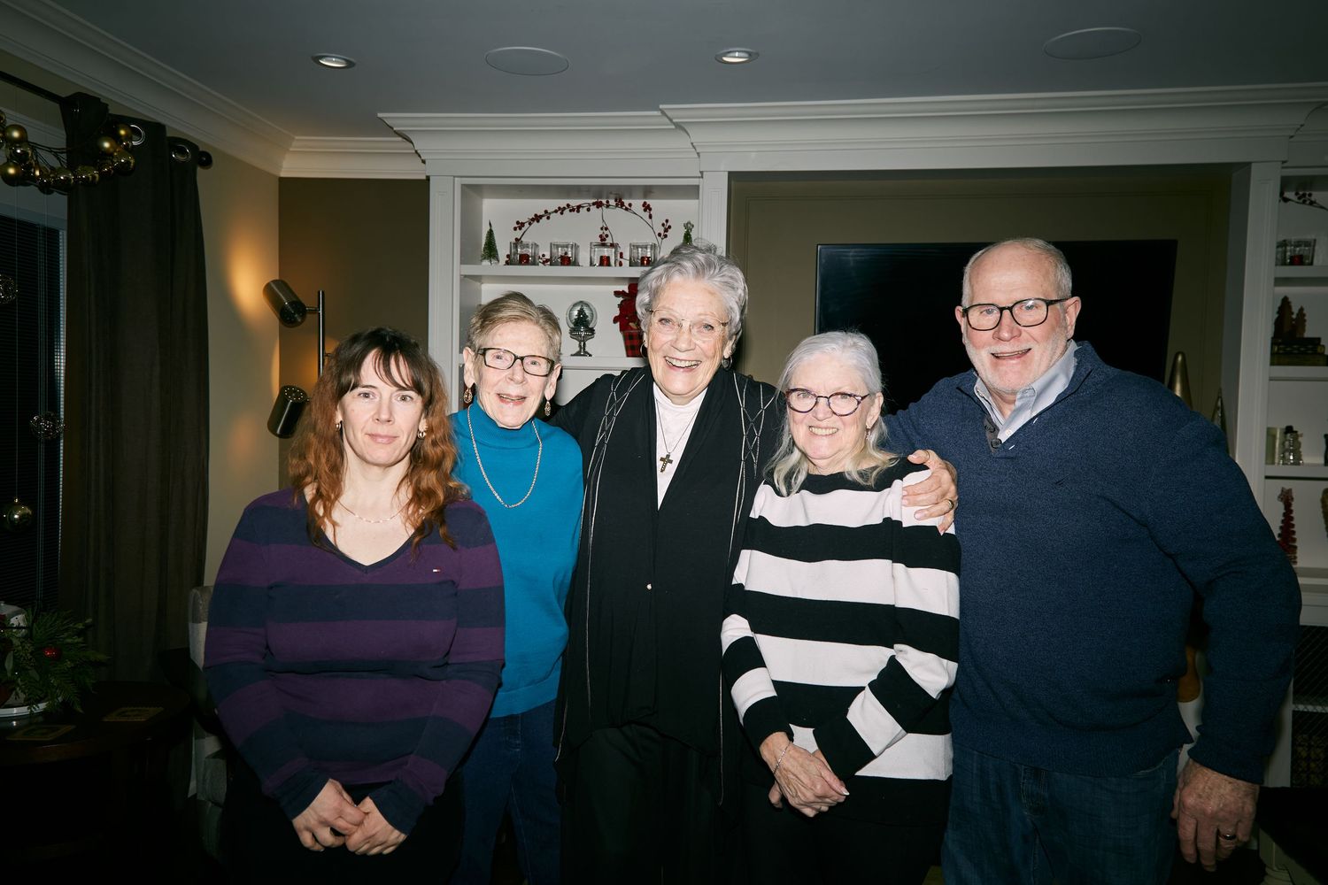 A group of five people standing together at an indoor gathering, wearing casual sweaters and smiling for the camera.
