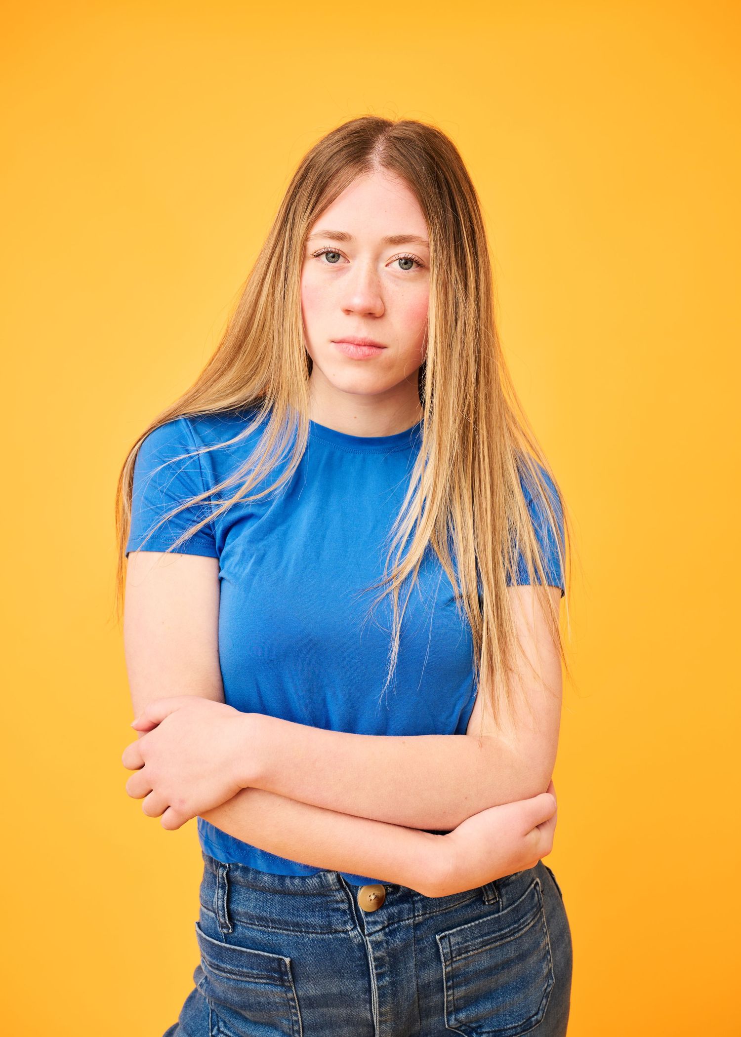 Portrait against yellow background of person in blue t-shirt and jeans with crossed arms.