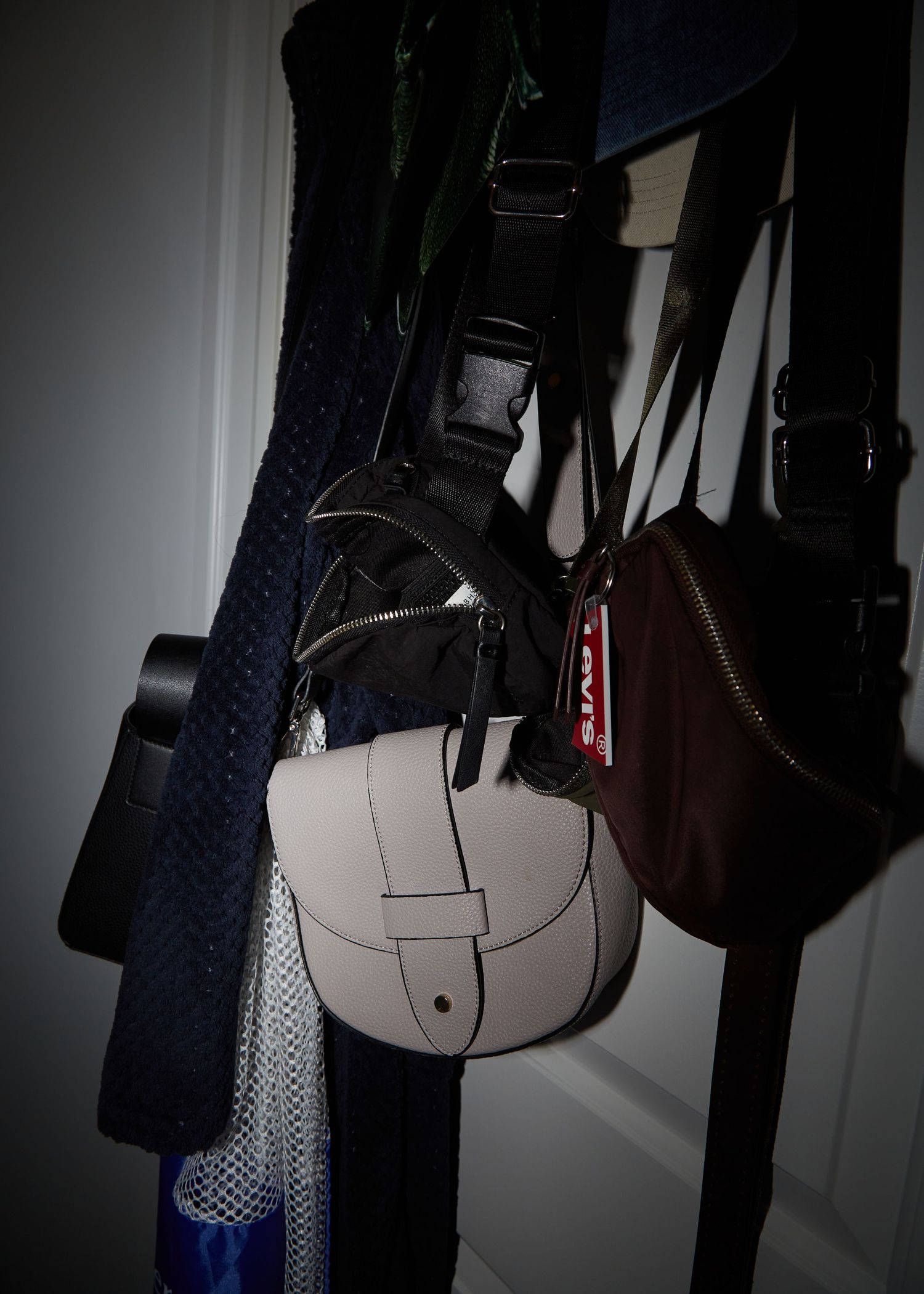 Dark closet with various handbags and accessories hanging on hooks.
