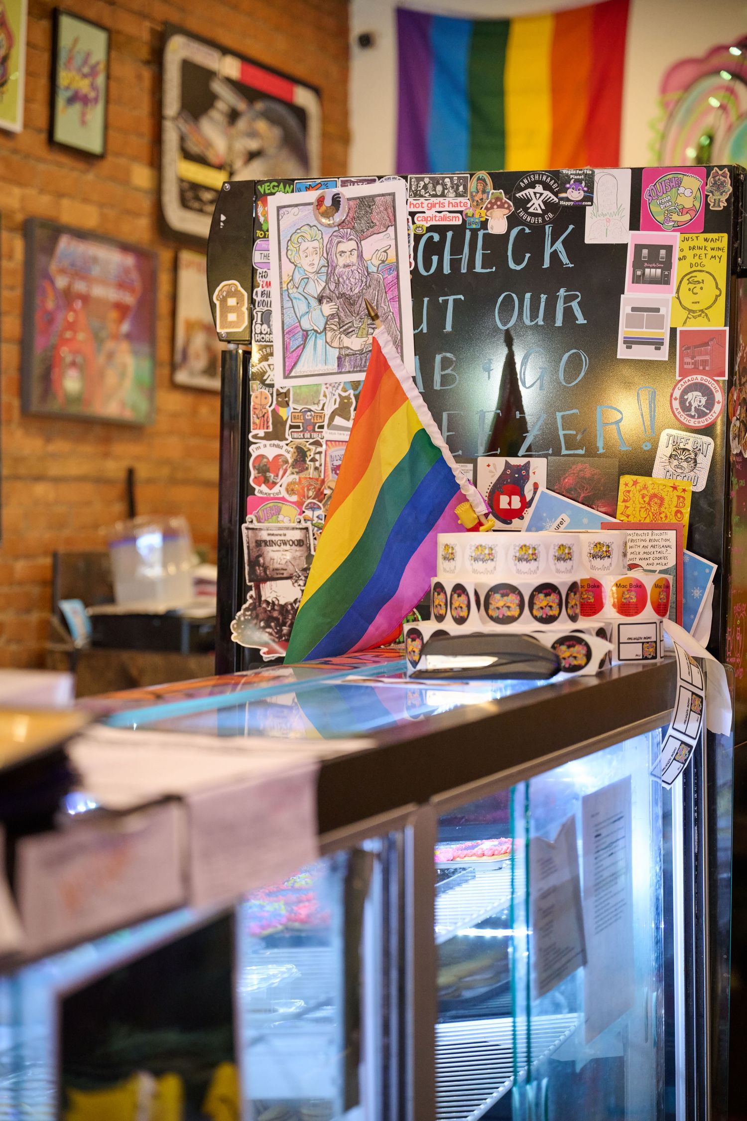 Rainbow pride flags and colorful stickers adorn a counter display in an LGBTQ-friendly cafe.
