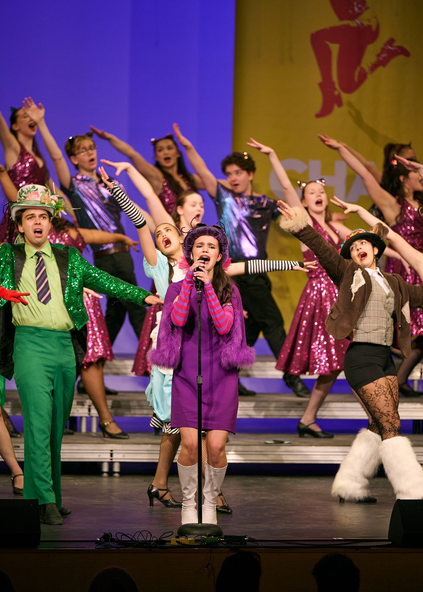 Young performers in colorful costumes sing and dance on stage during a vibrant show choir competition performance.