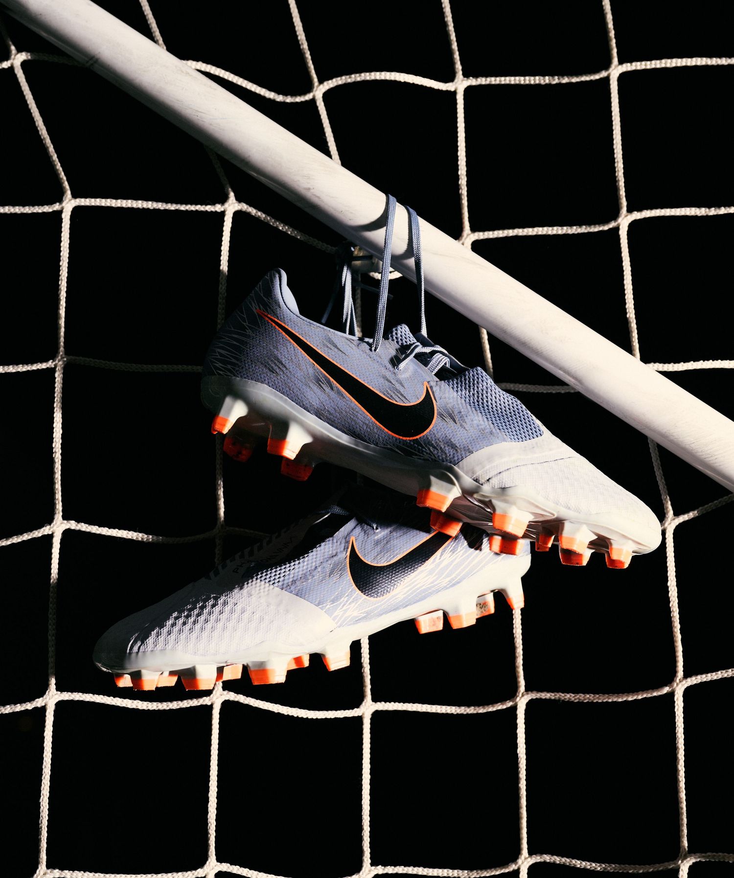 White Nike soccer cleats hanging on a goal net with dramatic lighting.