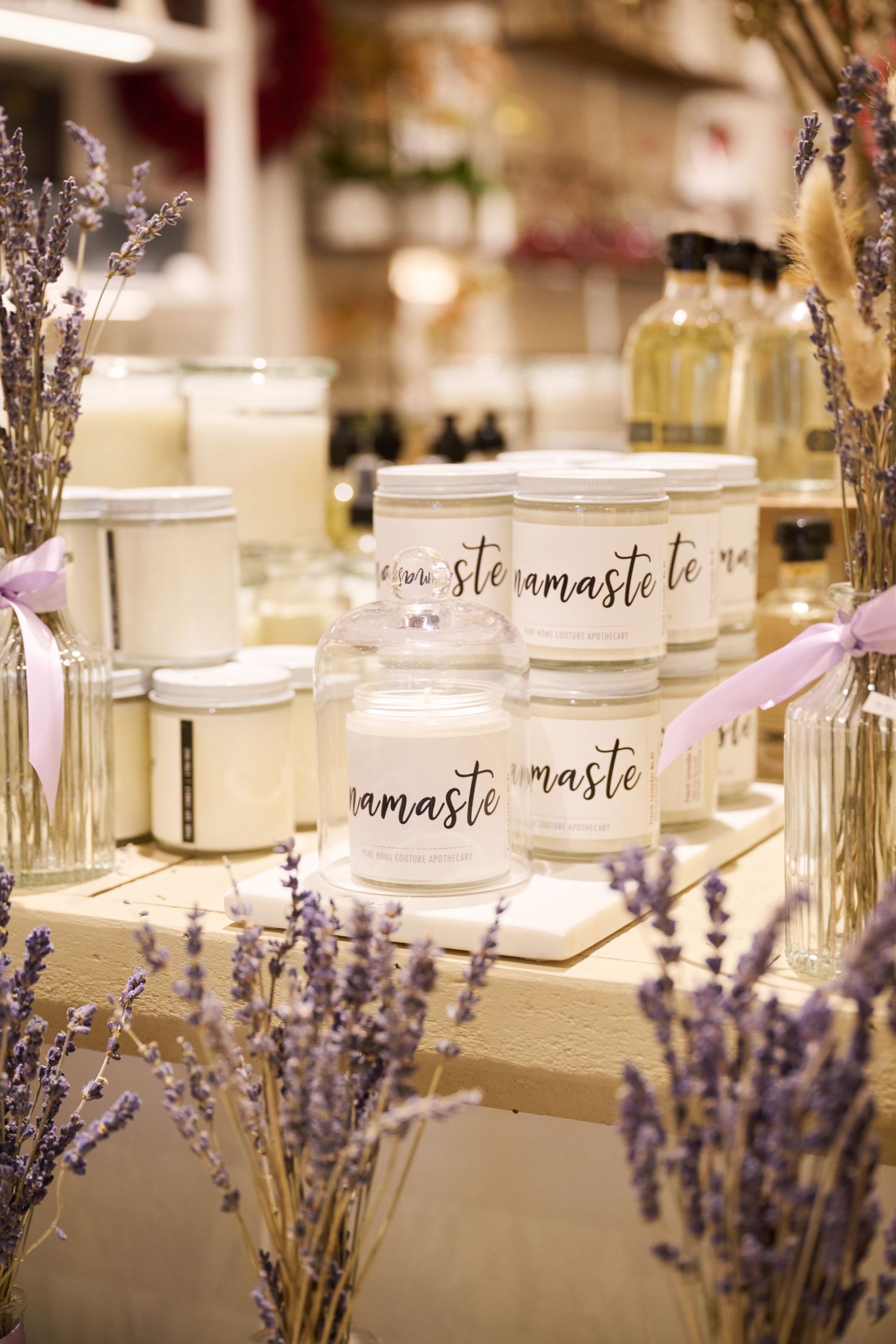 Namaste-labeled candles surrounded by dried lavender sprigs and glass bottles on a soft-lit display table.